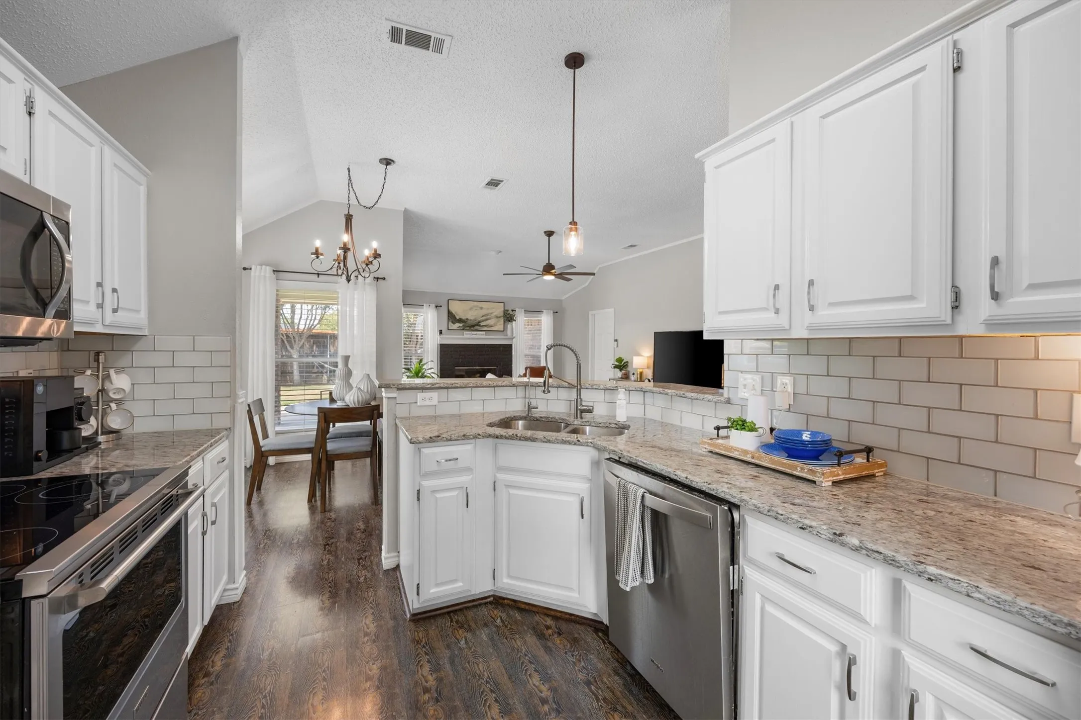Kitchen featuring white shaker-style cabinetry, gooseneck faucet, pendant lighting, granite countertops, white subway tile backsplash, stainless steel appliances, and wood-finish flooring