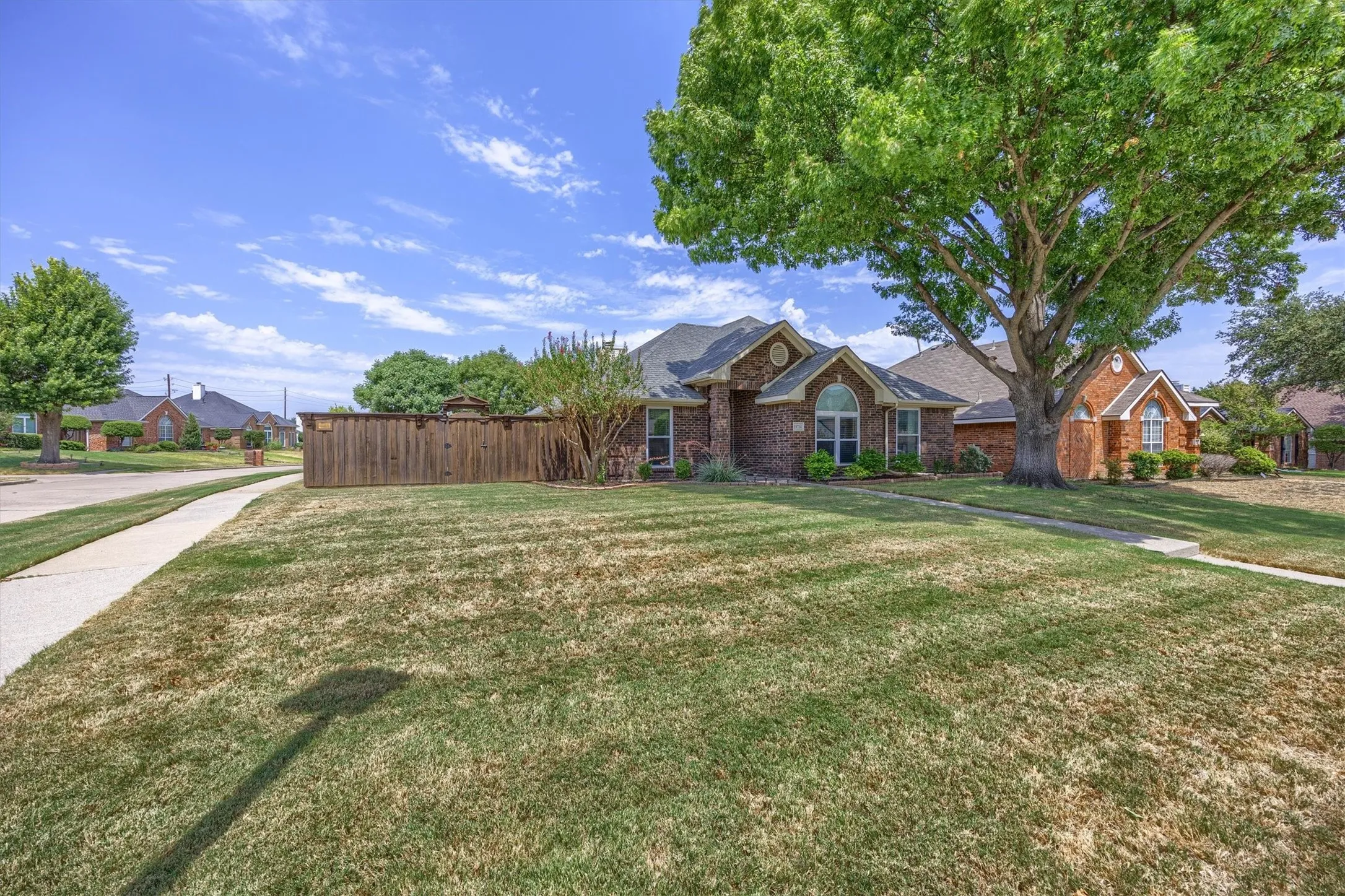 Brick Colonial estate showcasing a sprawling manicured lawn, mature shade trees, and wooden privacy fencing