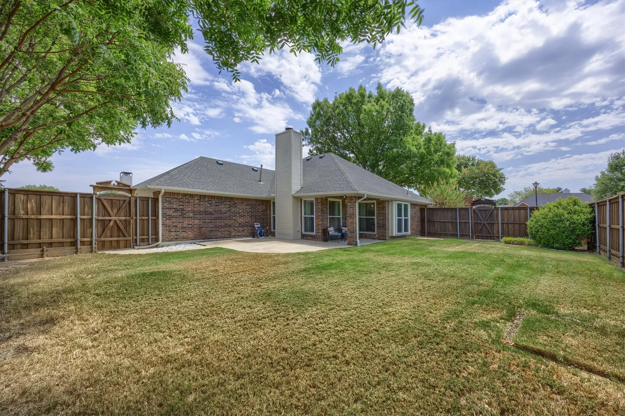 Expansive backyard featuring a brick exterior, a concrete patio, a wood board on board privacy fence, and mature trees