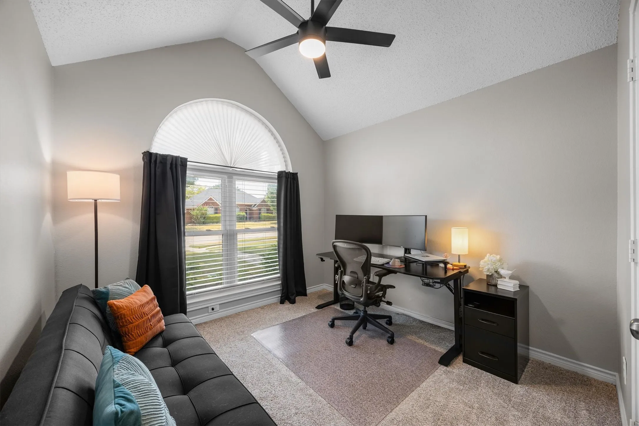 3rd bedroom being used as an office, with vaulted ceiling with a ceiling fan, arched window with blinds, carpeted flooring, and neutral wall tones