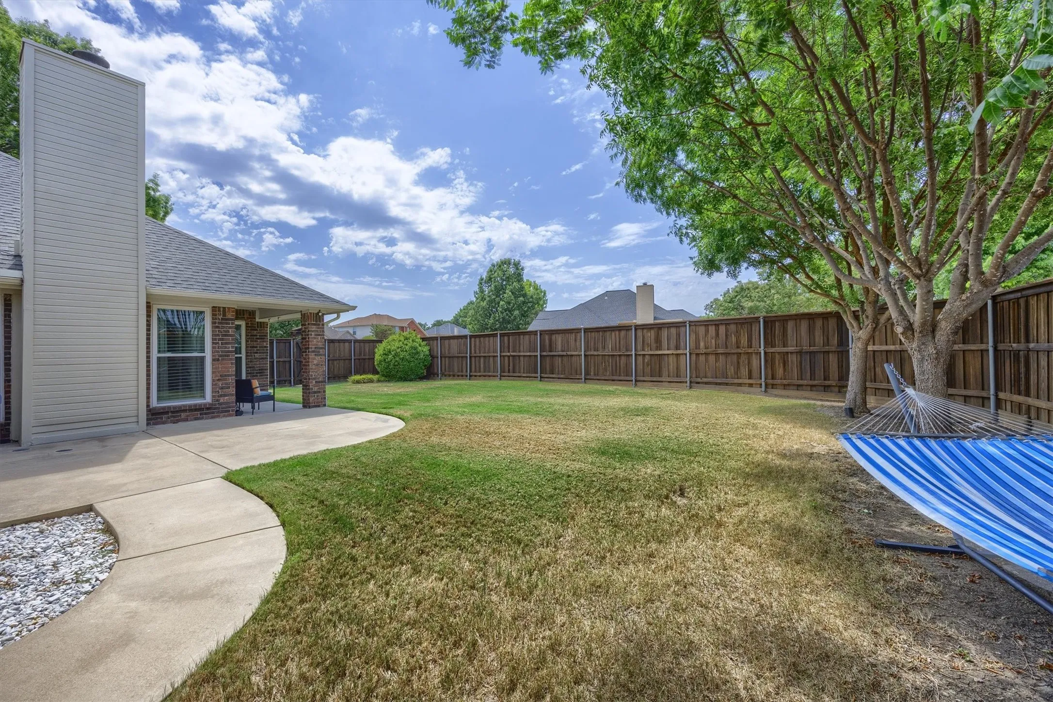 Expansive backyard featuring a covered patio, concrete pathway, and wood privacy fencing