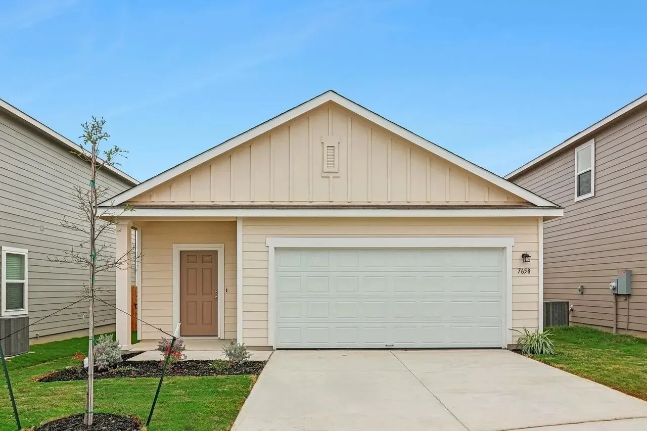Single-story residence featuring light-colored siding, an attached garage, a paneled front door, and a concrete driveway