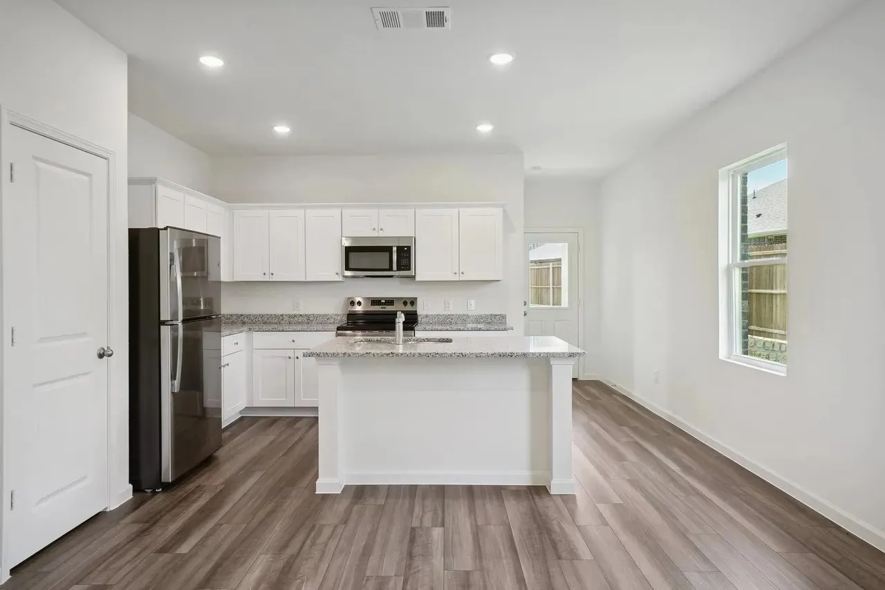 Open-concept kitchen with white cabinetry, stainless steel appliances, speckled countertops, and wood-finish flooring