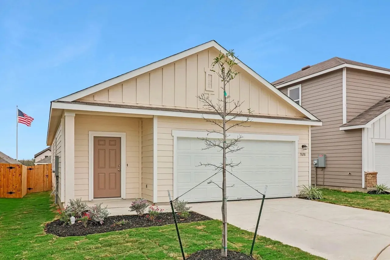Single-story residence featuring light-colored siding, a brown paneled front door, an attached garage, a concrete driveway, and a fenced backyard