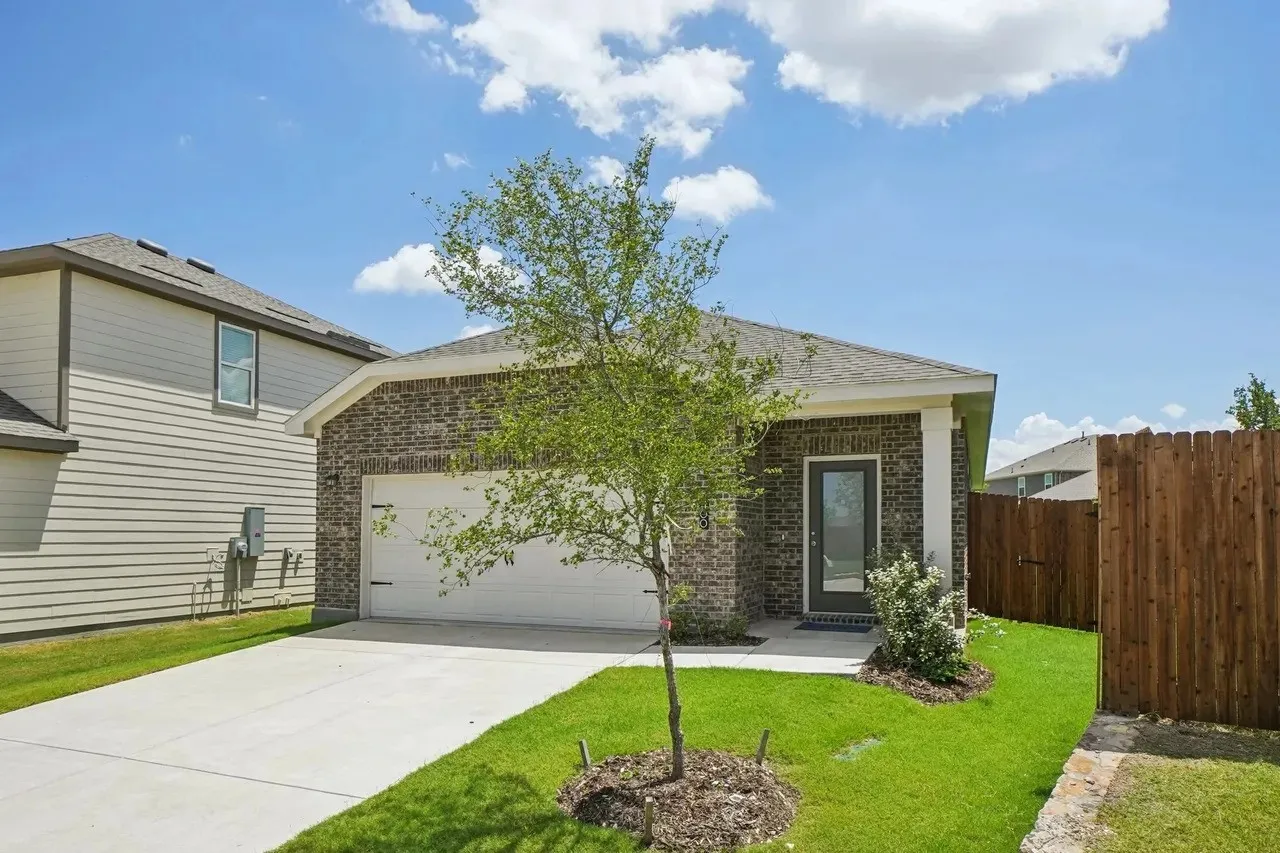 Brick facade with a white trim entry, attached garage, concrete driveway, and a wood fence
