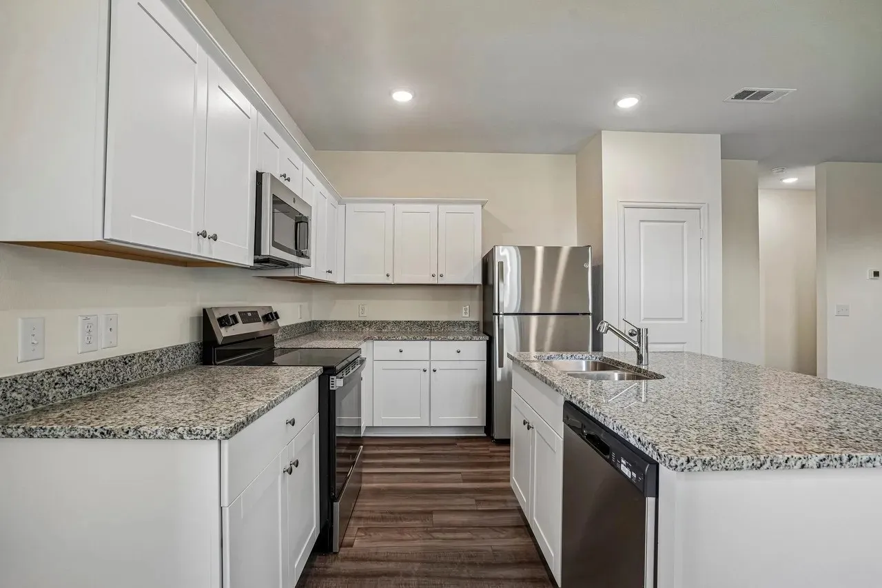 White shaker-style cabinetry, granite countertops, stainless steel appliances, wood-finish flooring, and recessed lighting
