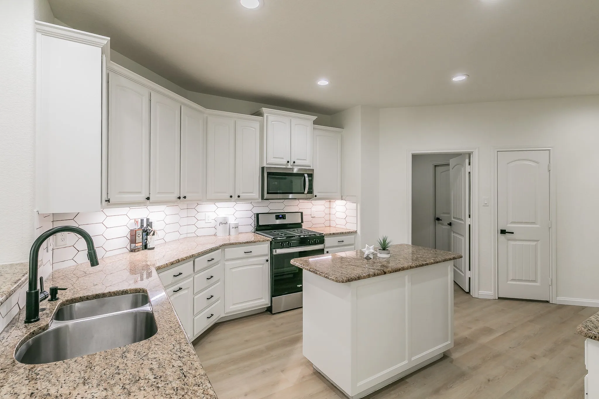 Large kitchen with white cabinets, an island, granite countertops, under cabinet lighting & a pantry