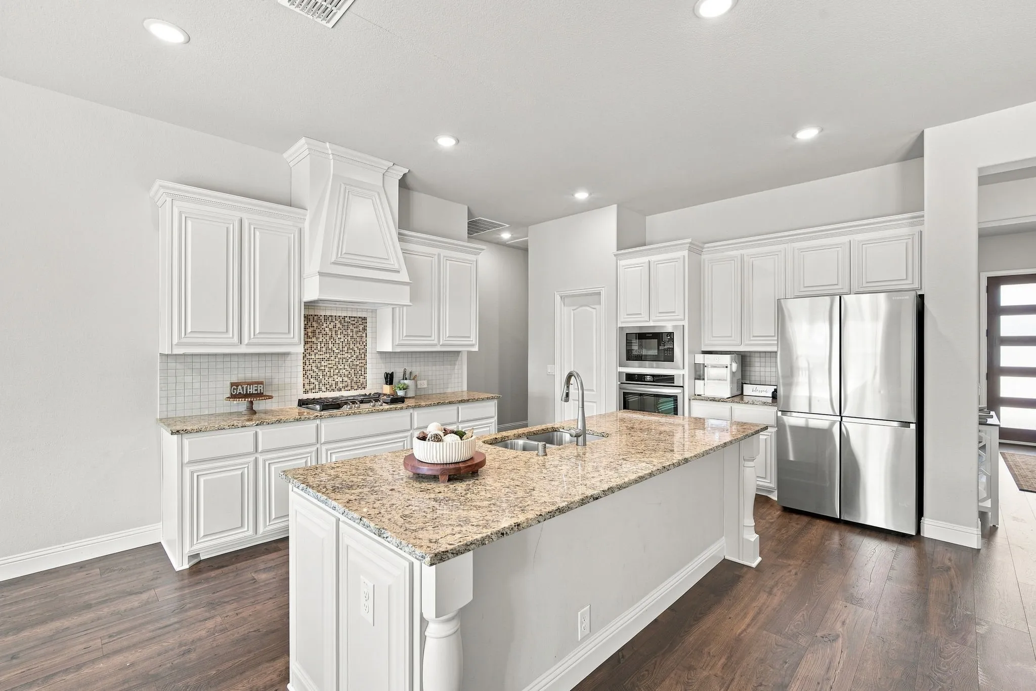 Equipped with built-in stainless steel appliances, a gas cooktop, a custom wood vent hood, and designer backsplash