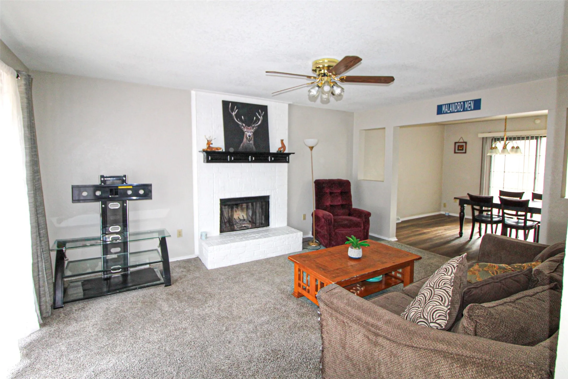 Living area featuring a white brick fireplace with a mantel, carpeted flooring, and a ceiling fan