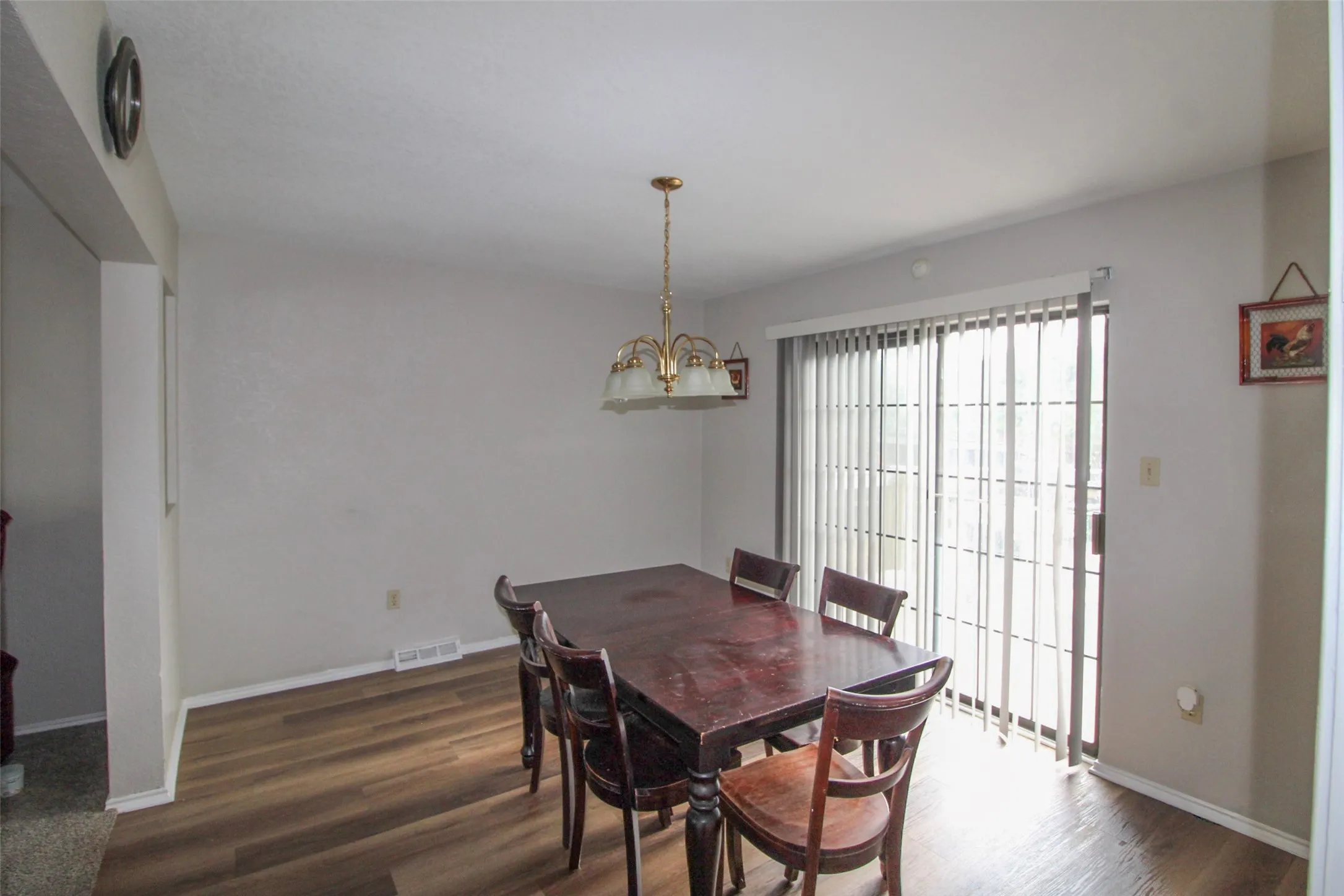 Wood-finish flooring, sliding glass door, and a brass-finish chandelier with frosted glass shades