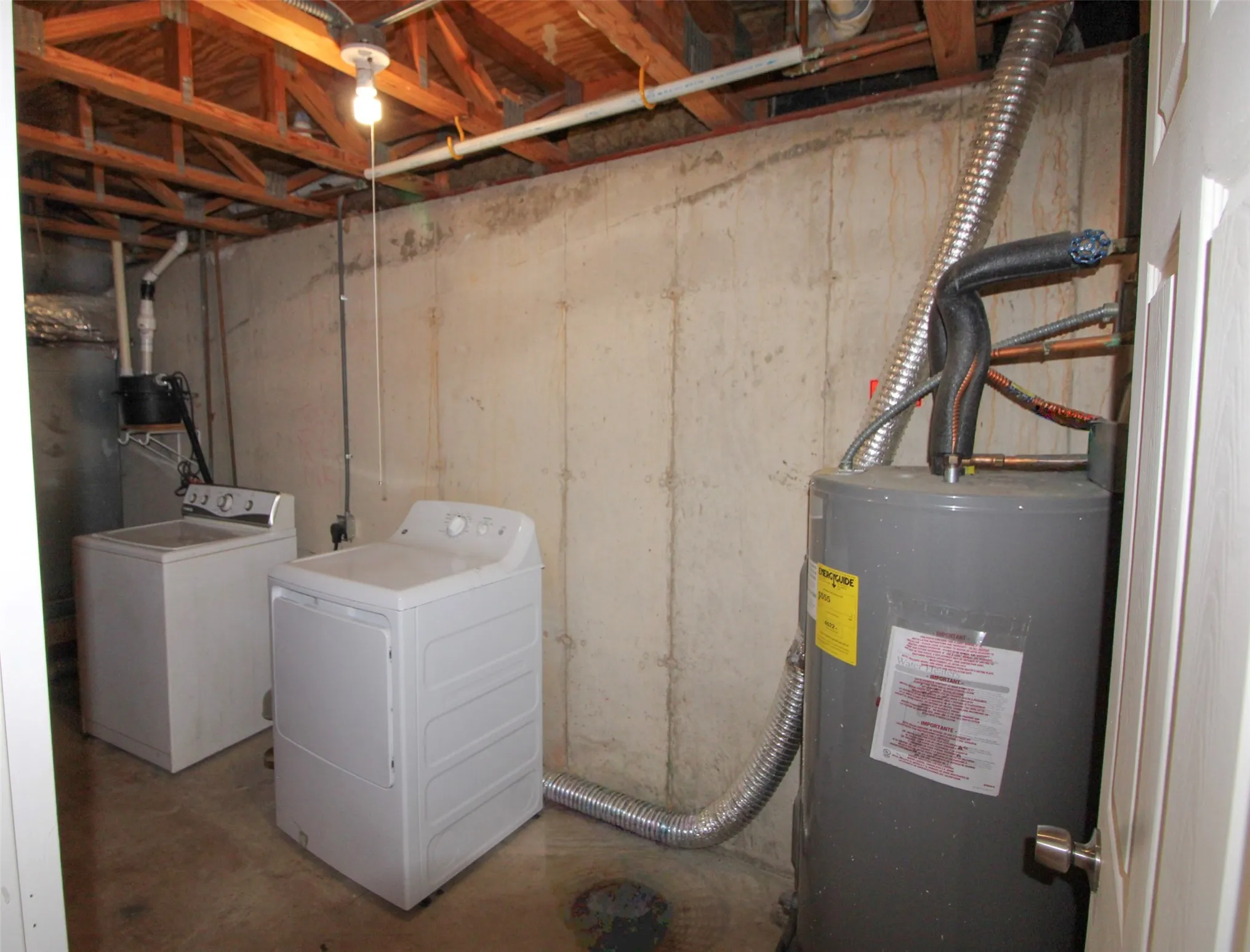 Unfinished basement with exposed ceiling joists and concrete walls, featuring a water heater and utility connections
