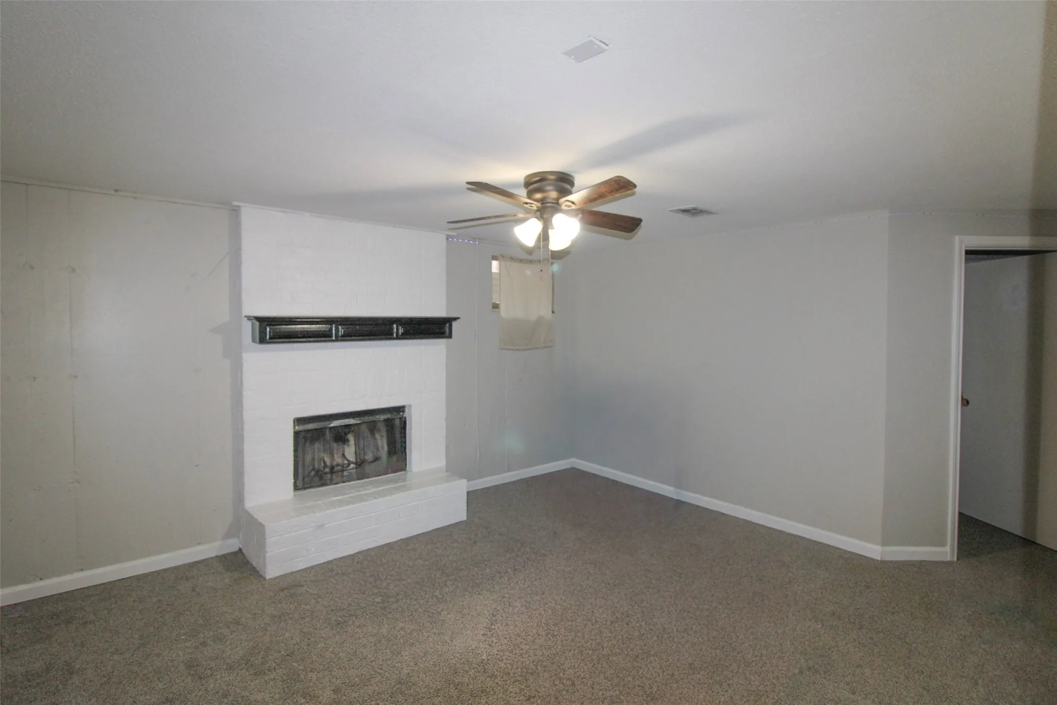 White painted brick fireplace with a dark mantel, ceiling fan with light fixture, and carpeted flooring