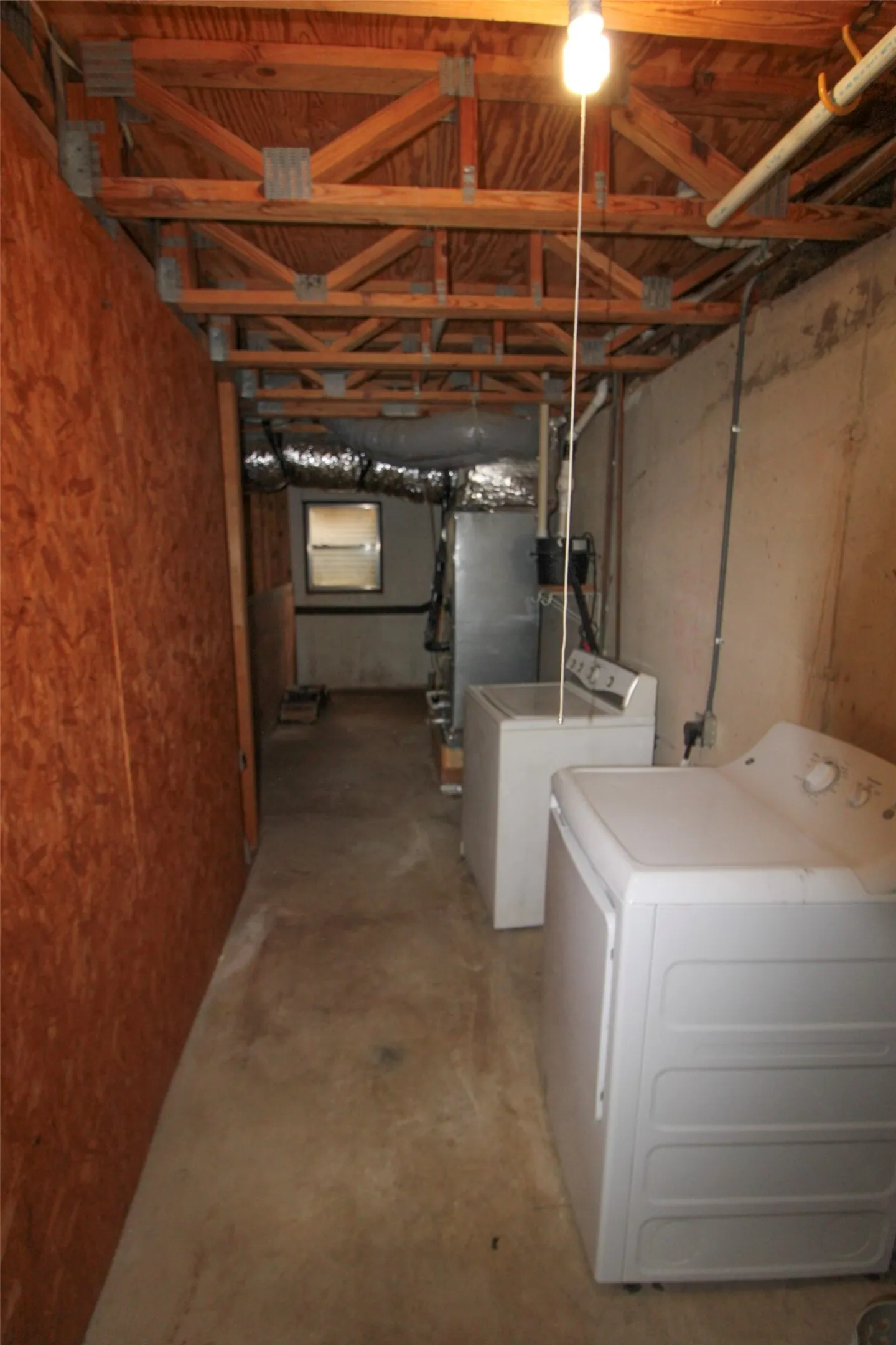 Unfinished basement featuring exposed wood trusses, a utility window, and concrete flooring