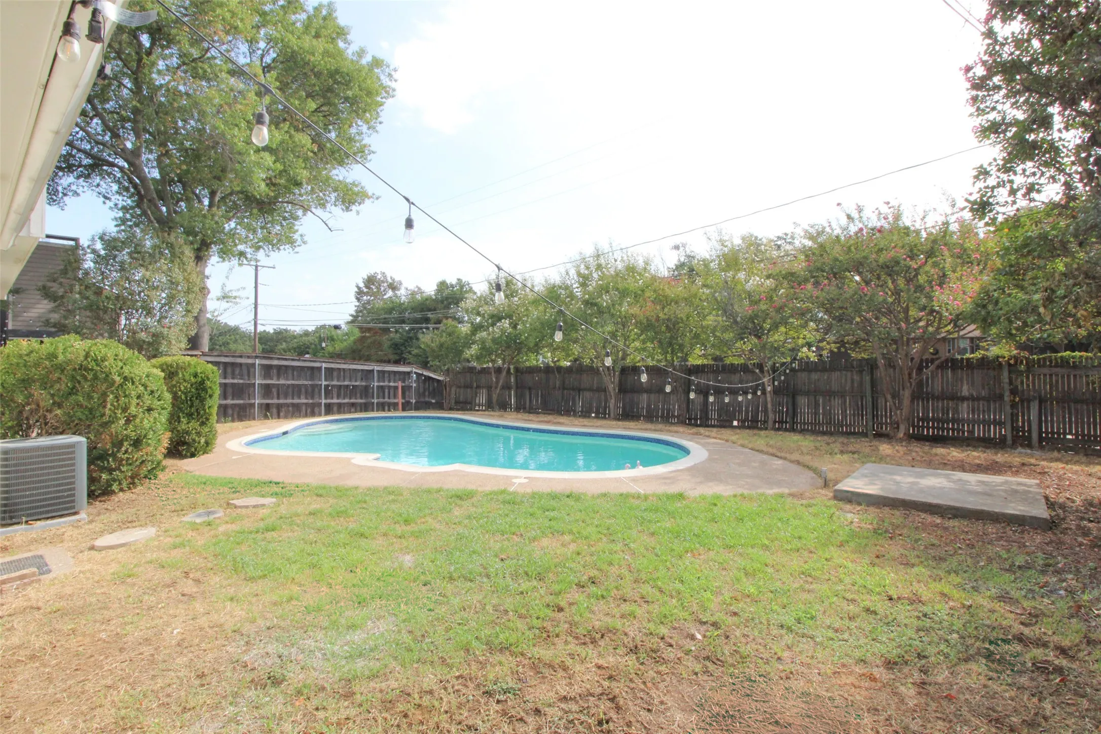 Private backyard featuring a swimming pool, concrete pool deck, and wood privacy fence