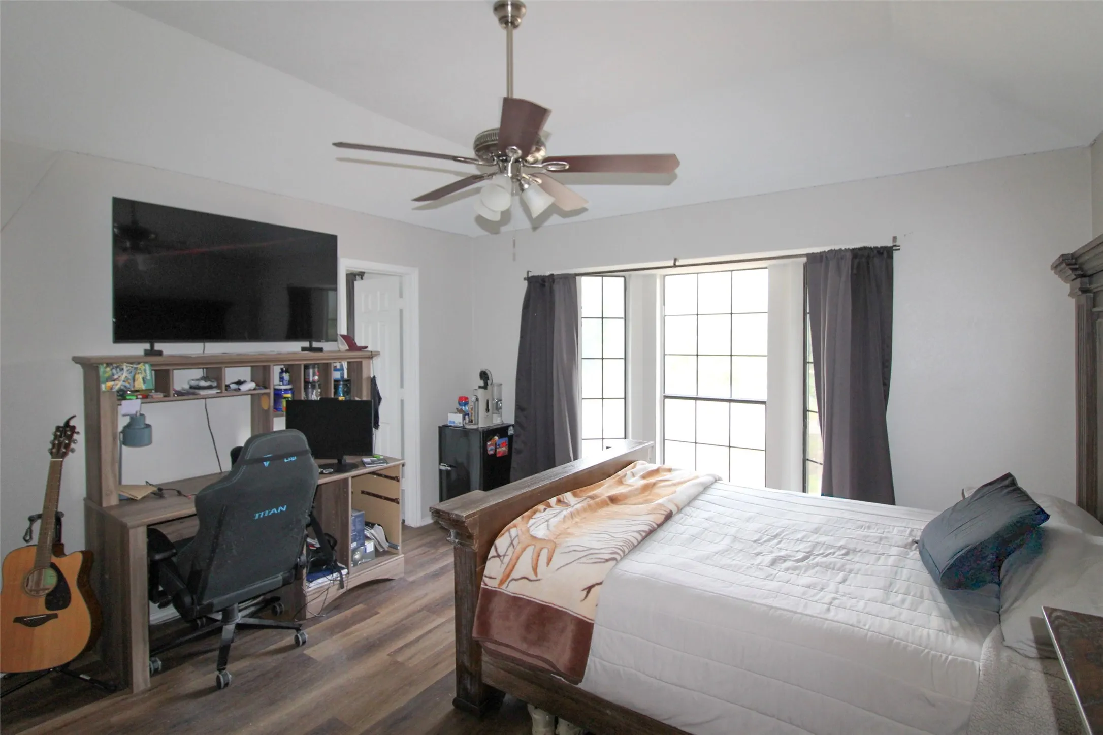 Vaulted ceiling with a ceiling fan, wood-finish flooring, and a large window with grid pattern