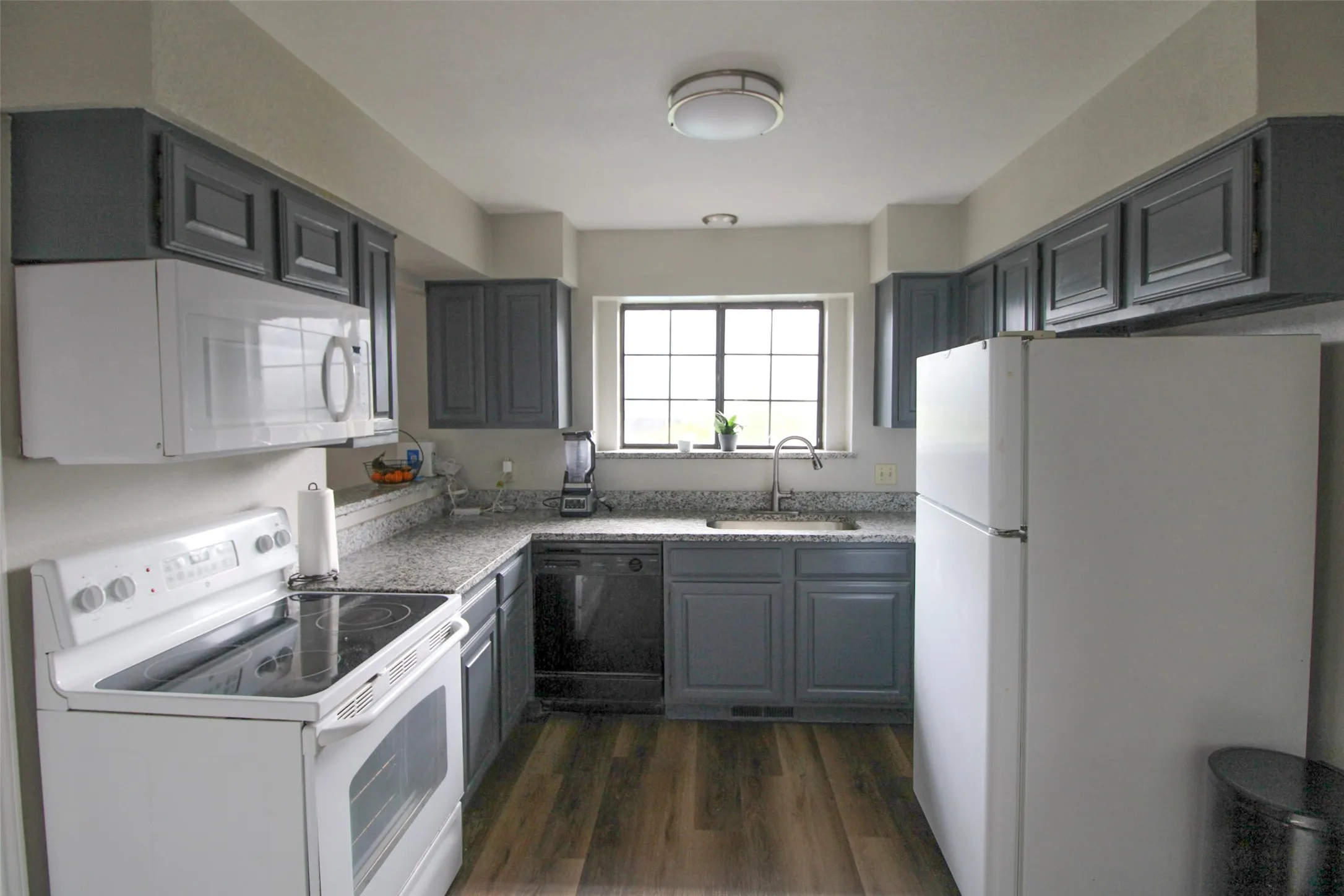 U-shaped kitchen featuring wood-finish flooring, gray cabinetry, light-toned countertops, and a window above the sink