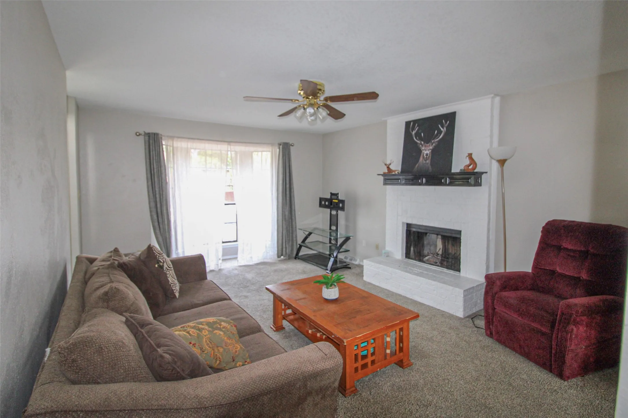 Living area with a fireplace, ceiling fan, and carpeted flooring
