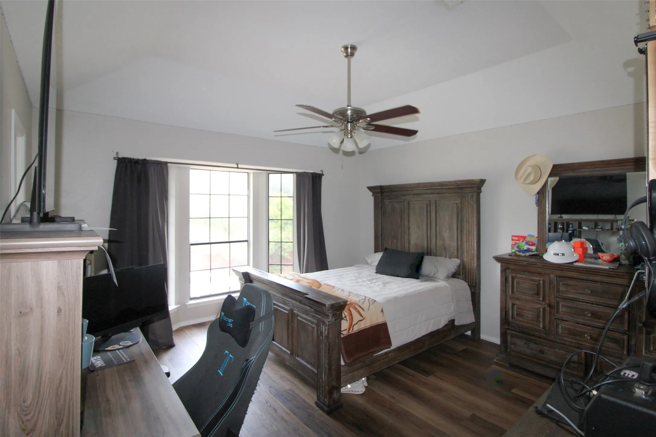 Tray ceiling with a ceiling fan, bay window with dark drapery, wood-finish flooring, and built-in wood-finish cabinetry