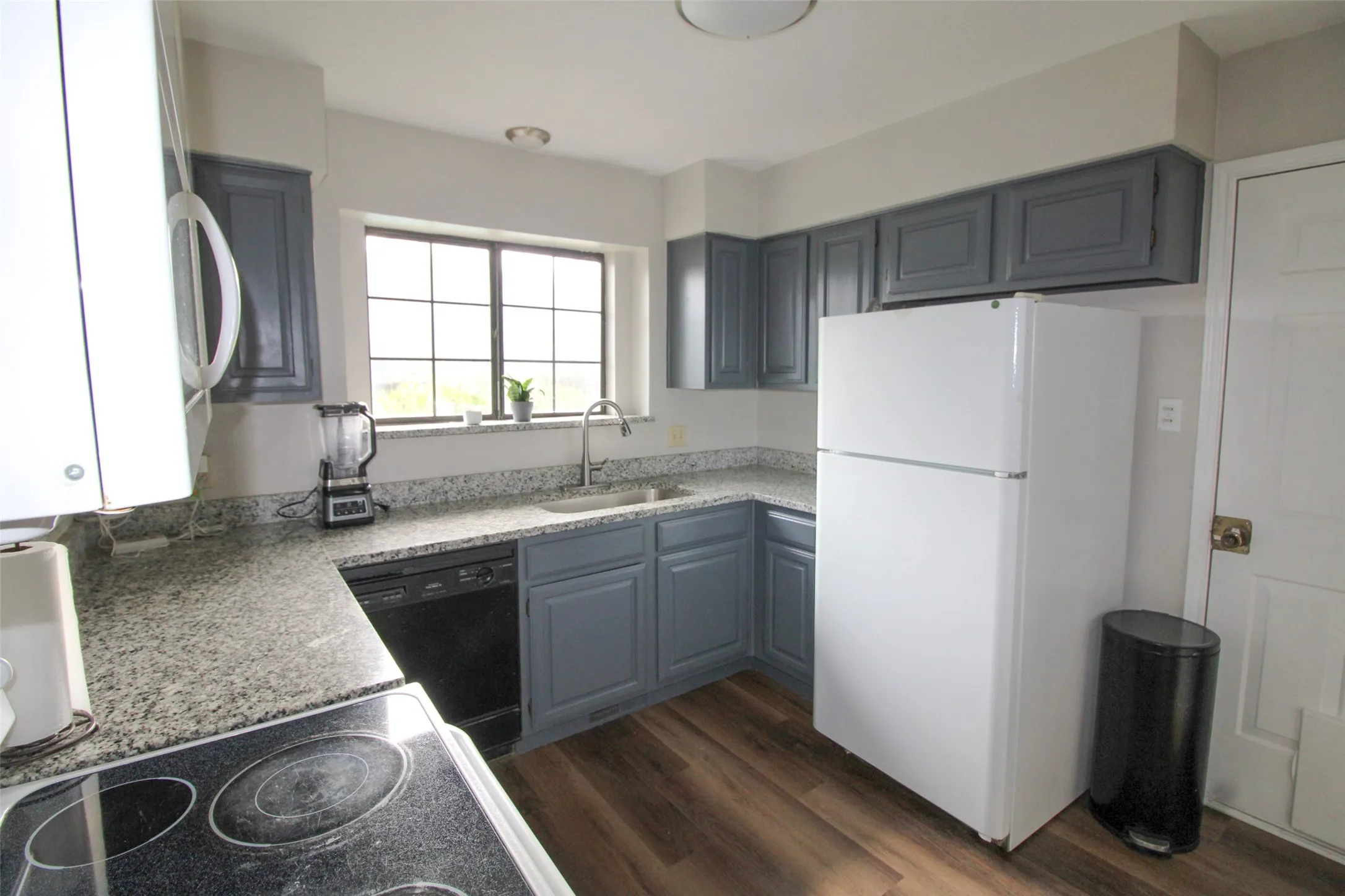 Kitchen featuring grey cabinetry, light-toned countertops, a window over the sink, wood-finish flooring, and a white refrigerator
