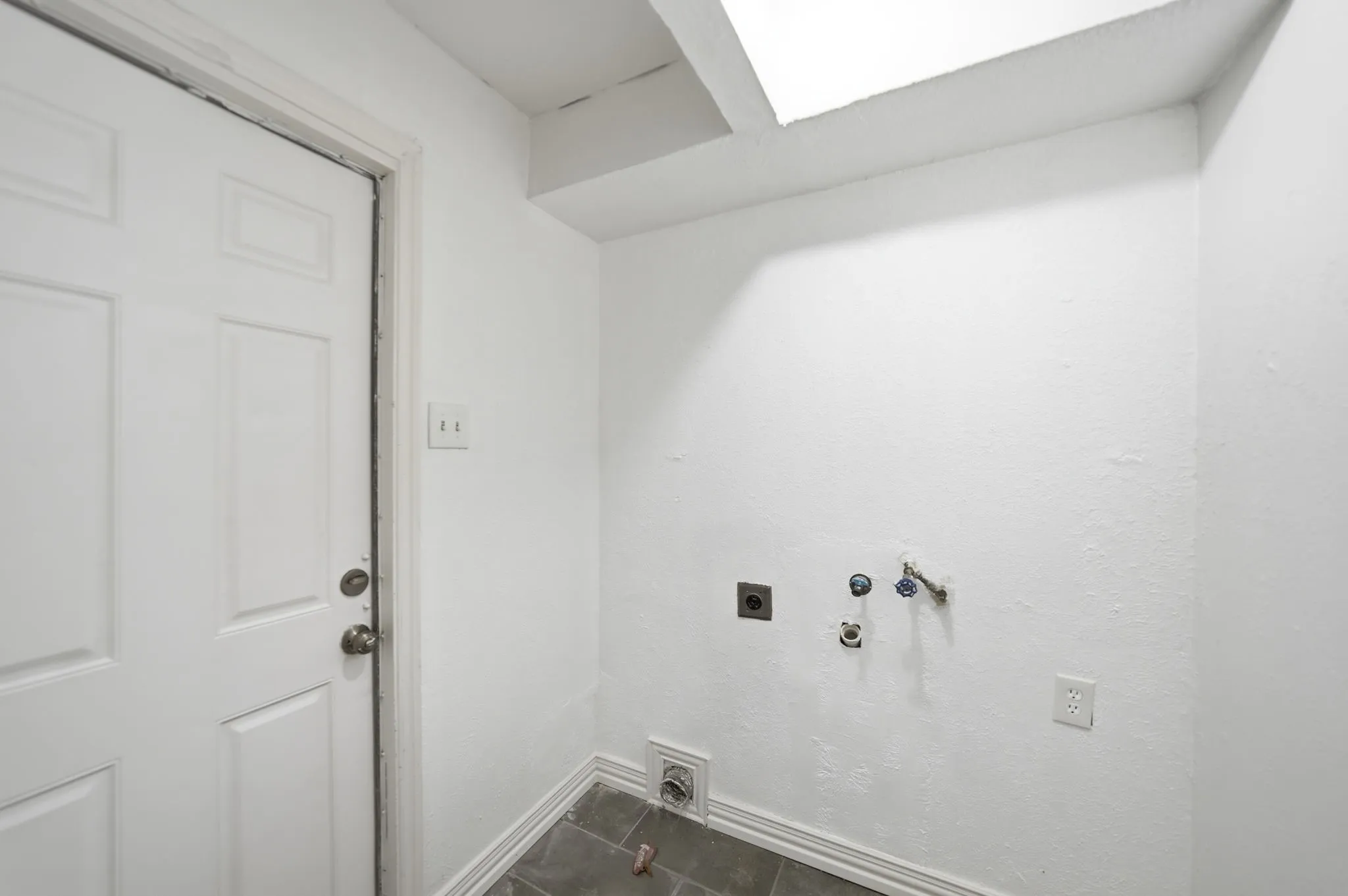 Utility space with panel door, wall-mounted electrical outlets, and plumbing connections