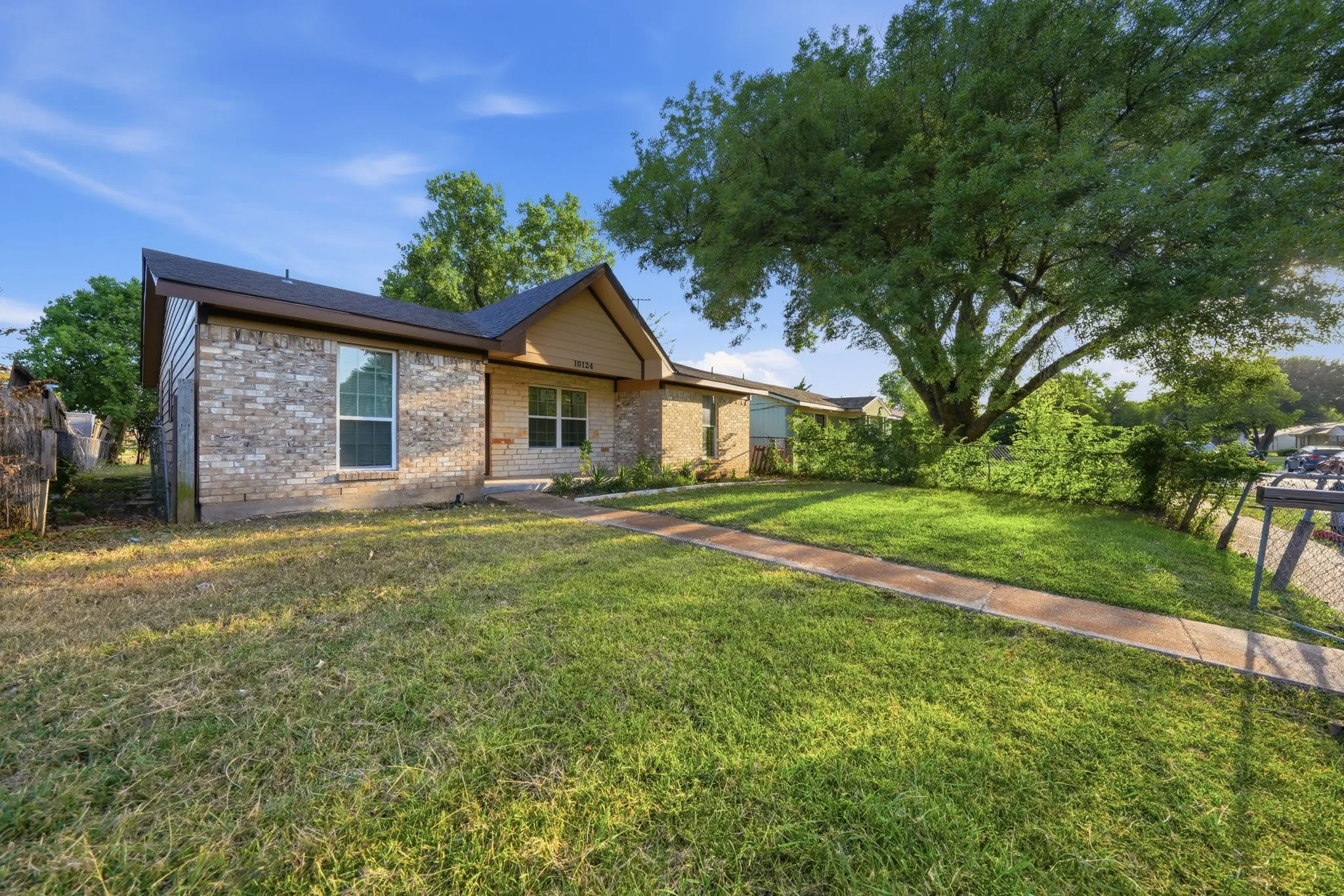 Brick exterior with contrasting siding accents, dark shingle roof, front yard with mature tree, and a concrete walkway