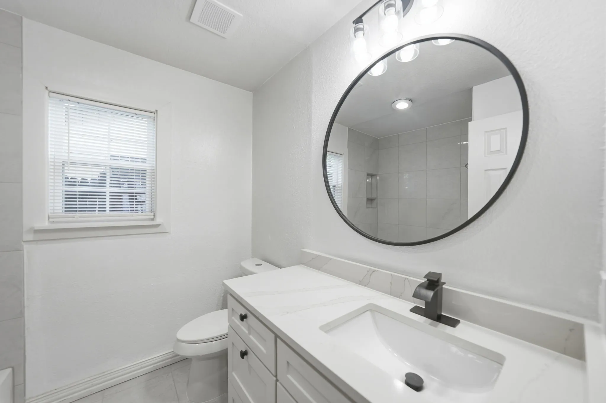 White vanity with dark hardware, a single integrated sink, and a light-toned countertop