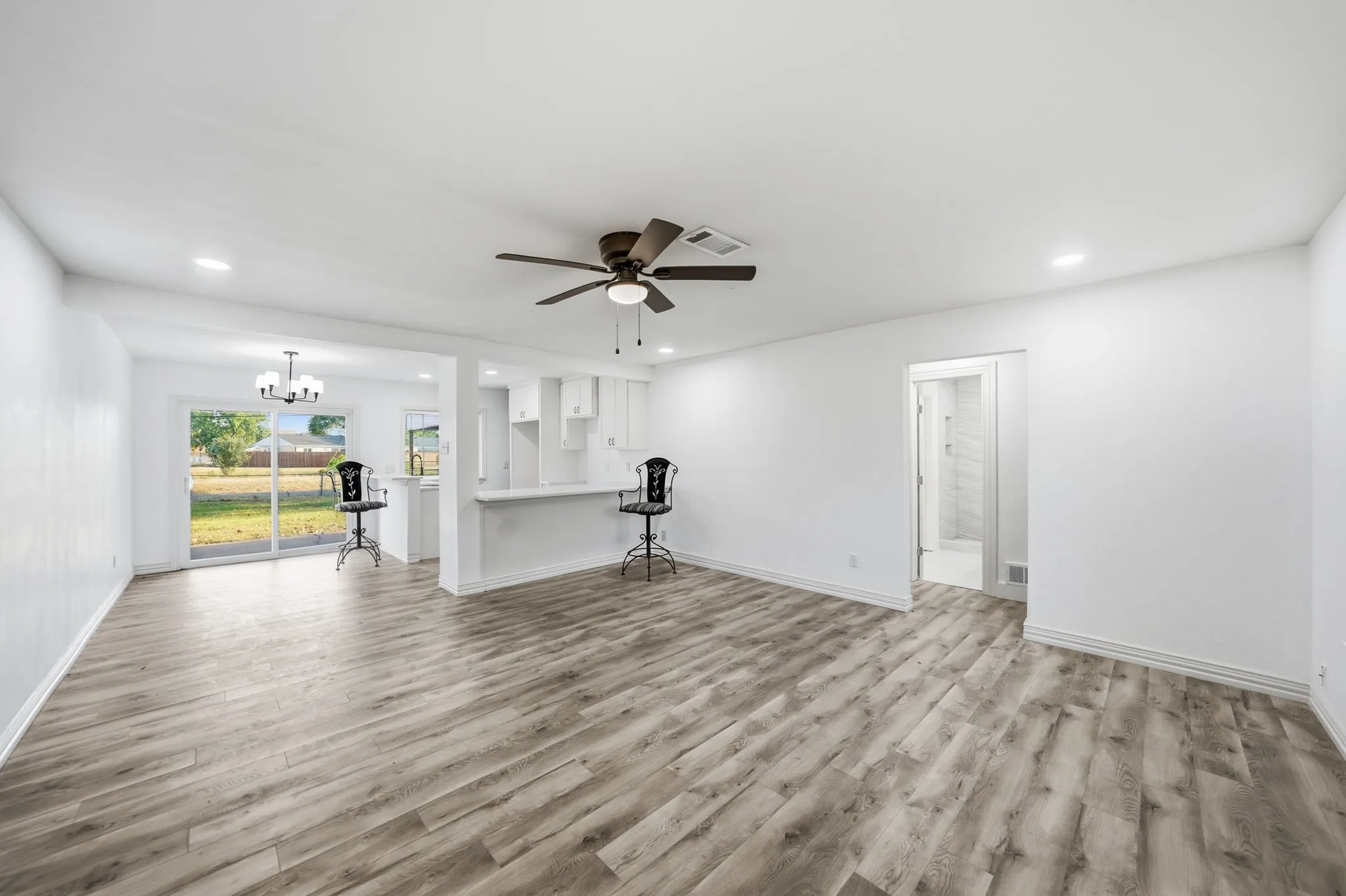 Wood-finish flooring, recessed lighting, ceiling fan, sliding glass door, and a kitchen pass-through with a breakfast bar