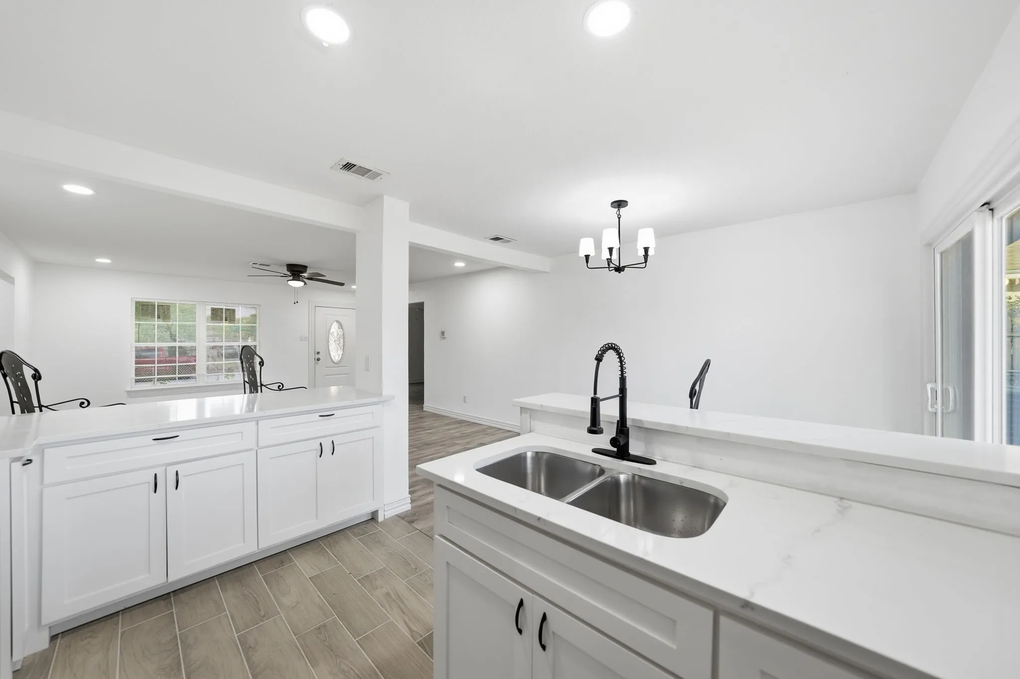 White shaker cabinetry, dual basin stainless steel sink, black gooseneck faucet, light-toned wood-finish flooring, and a sliding glass door