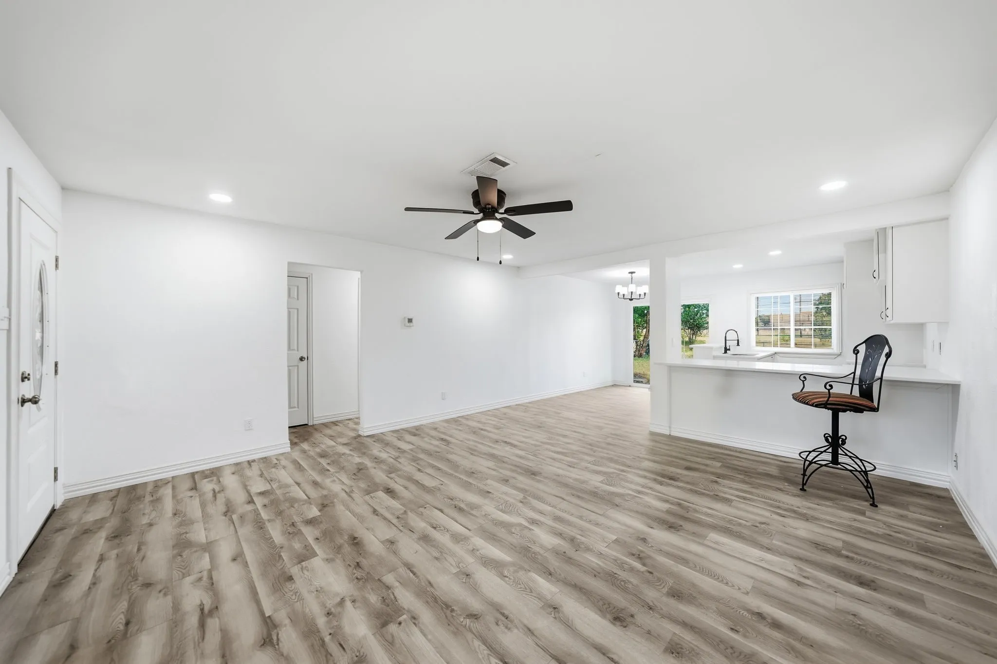 Wood-finish flooring, recessed lighting, ceiling fan, white cabinetry, and a kitchen sink with a window