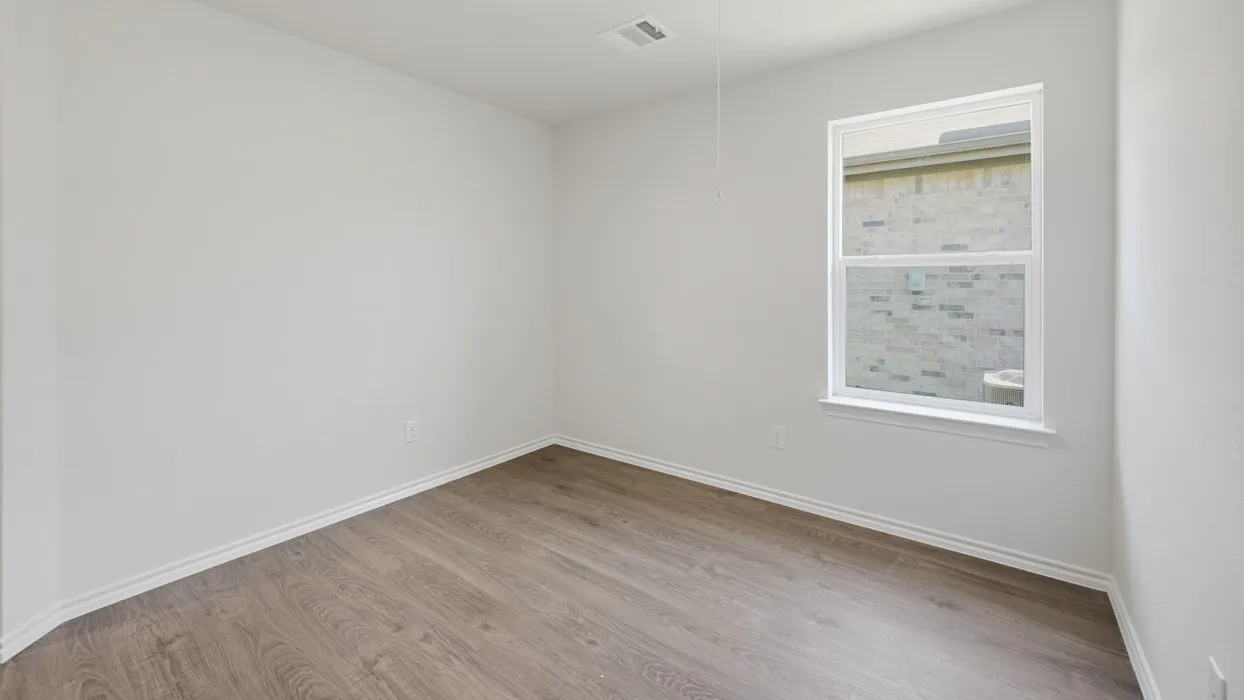 Bright bedroom featuring wood-finish flooring, clean white walls, and a large window with natural light