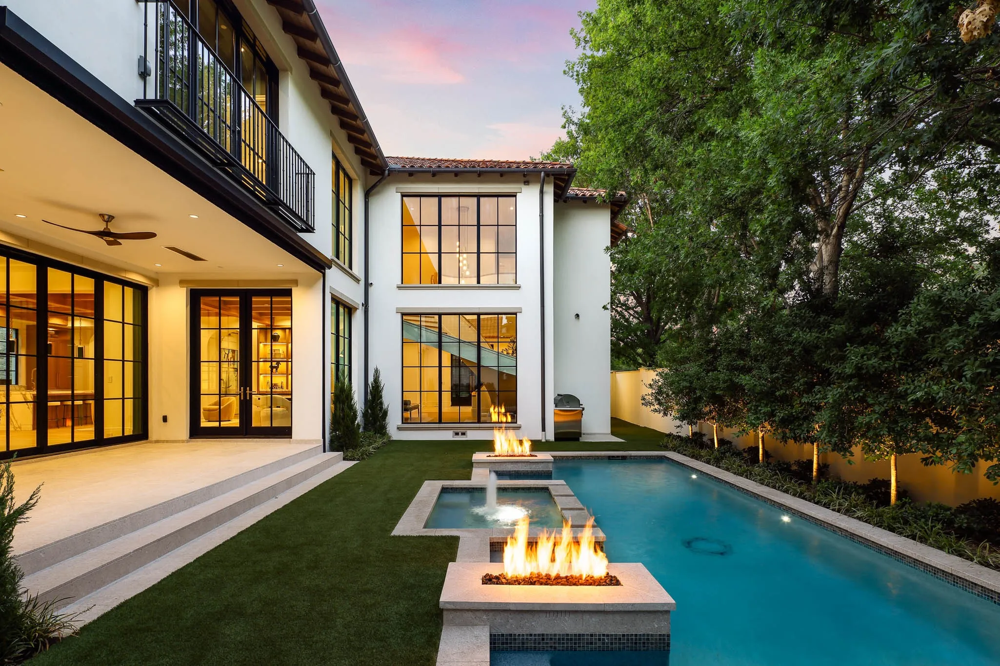 Outdoor pool and spa with water feature and linear fire accents open to landscaped backyard and climate controlled Loggia and built-in grill