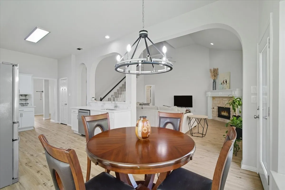 Open-concept living area featuring light wood-finish flooring, a contemporary chandelier, arched entryways, and a stone-faced fireplace with a mantel