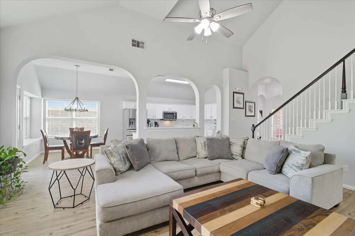Vaulted ceilings with a ceiling fan, wood-finish flooring, staircase with dark railing, arched doorways, and built-in window seating
