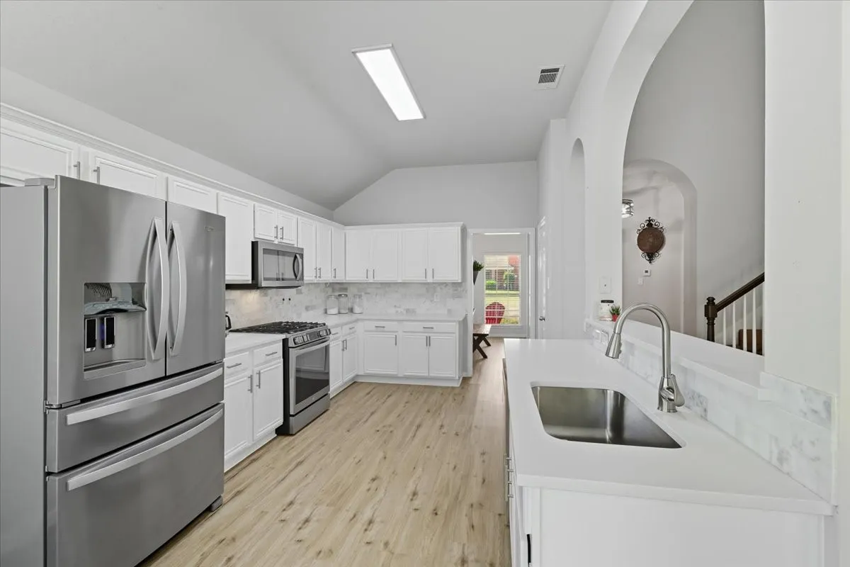 Kitchen featuring white cabinetry, stainless steel appliances, wood-finish flooring, and a single-basin sink with a gooseneck faucet