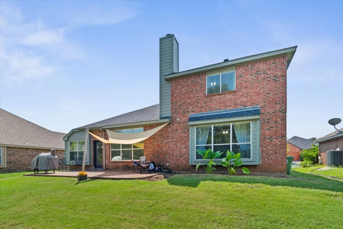 Brick exterior with a prominent chimney, a ground-level patio, and an expansive lawn