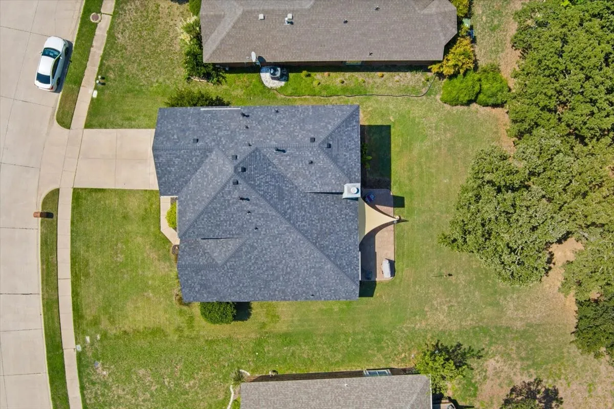 Asphalt shingle roof, paved driveway, concrete sidewalks, expansive grassy areas, and mature trees