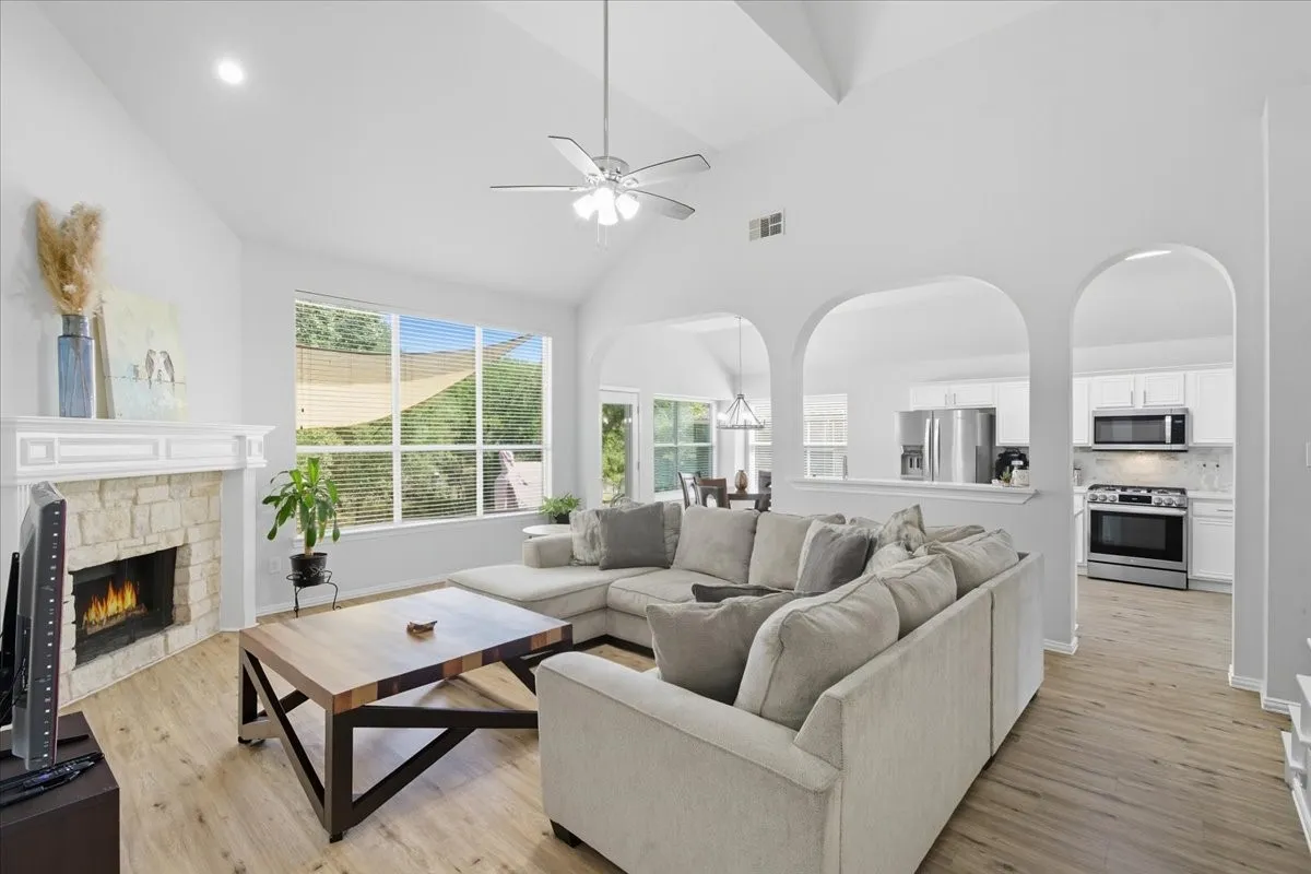 Vaulted ceiling with ceiling fan, stone-faced fireplace with mantle, wood-finish flooring, large window, and arched doorways
