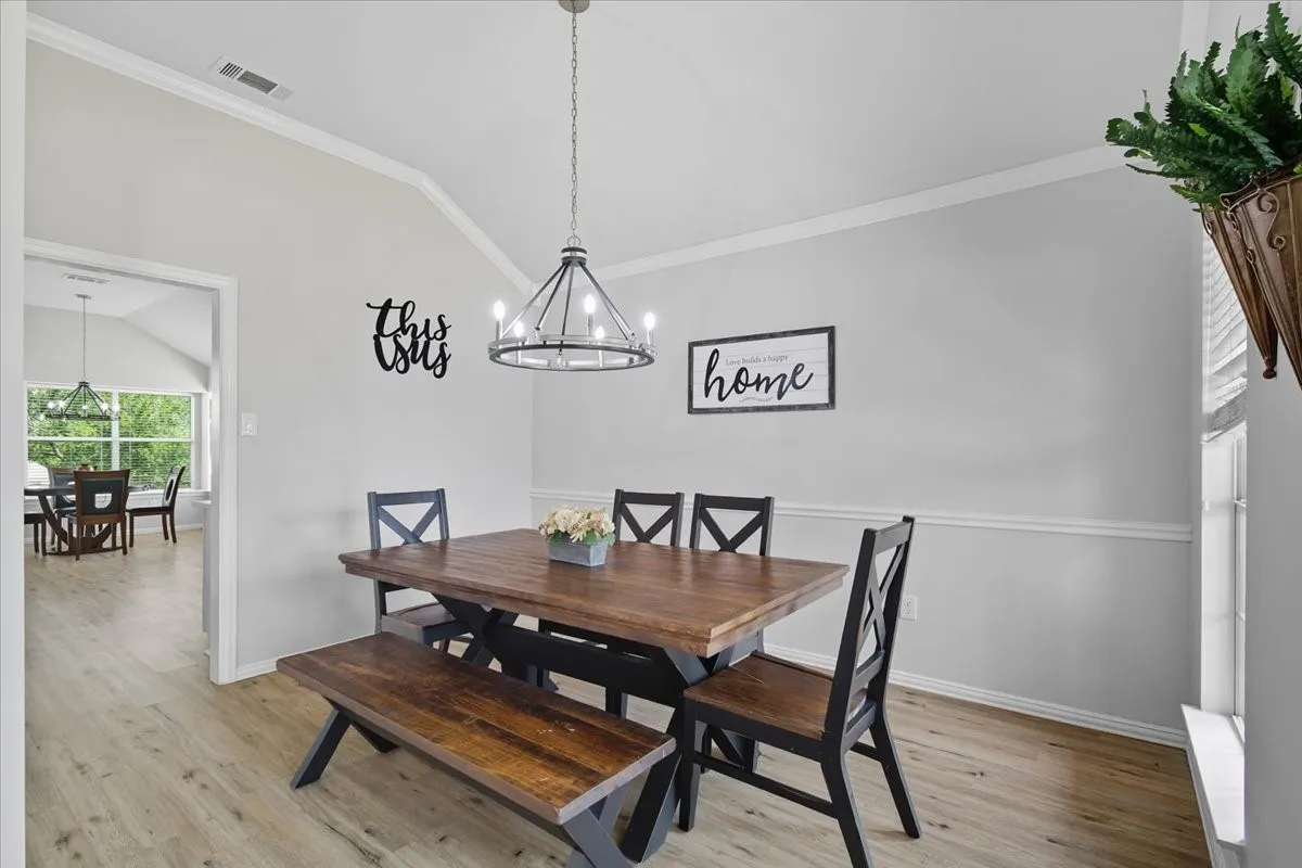 Vaulted ceiling with white crown molding, wood-finish flooring, two-tone wall treatment, and a dark metal chandelier