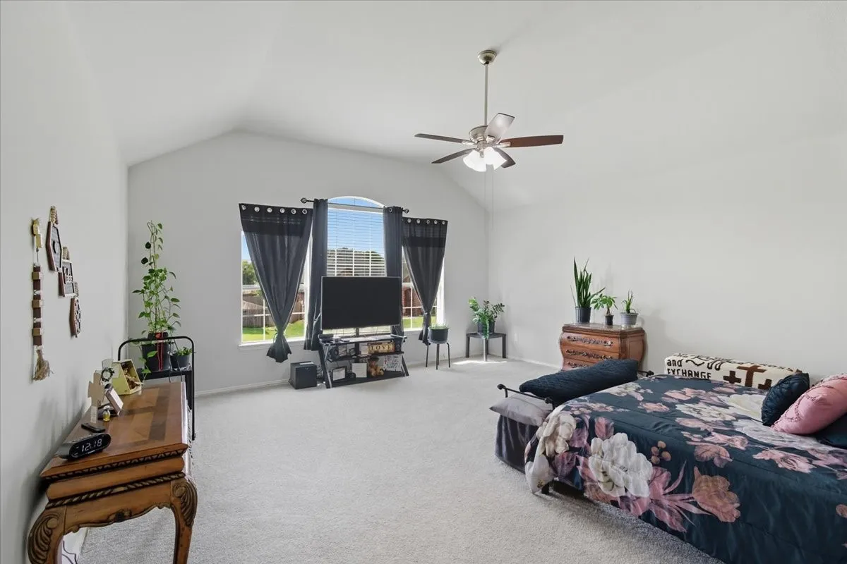Vaulted ceiling, ceiling fan with light fixture, arched window, and light-colored carpet flooring
