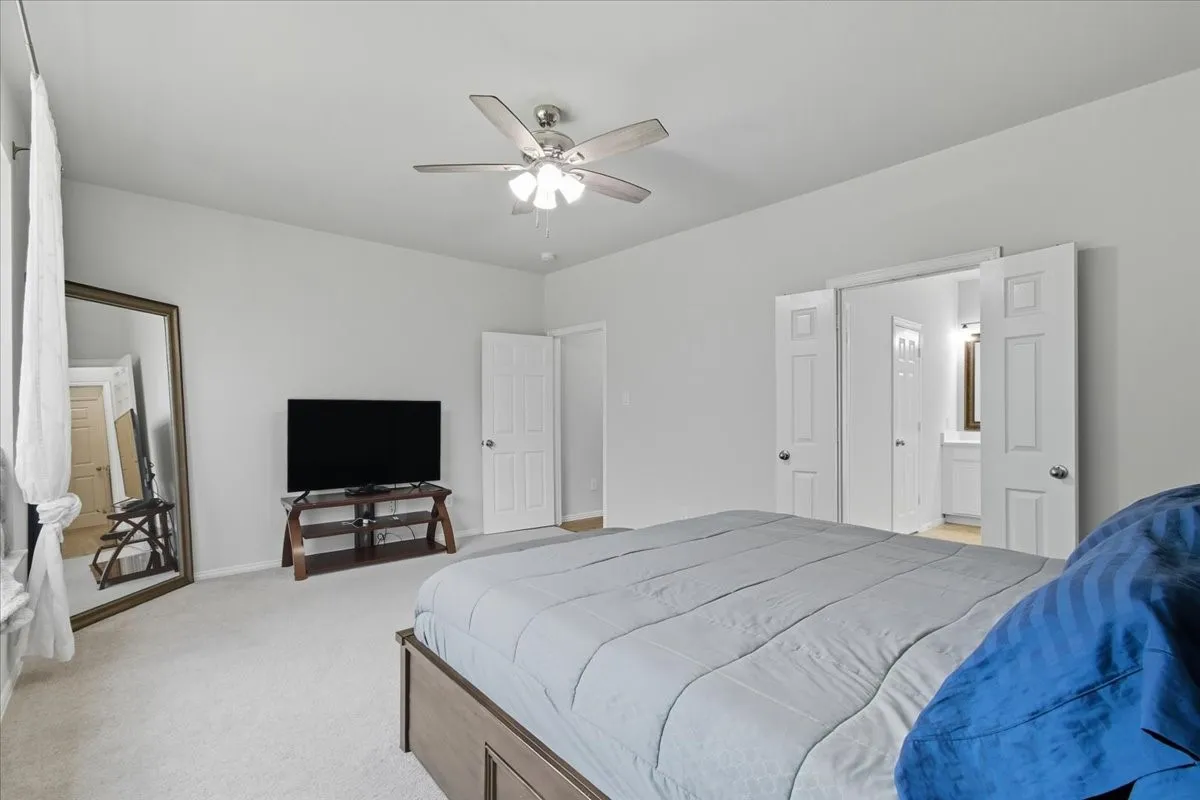Ceiling fan with integrated lighting, neutral wall tones, carpet flooring, double panel doors, and an en-suite bathroom with a vanity and mirror