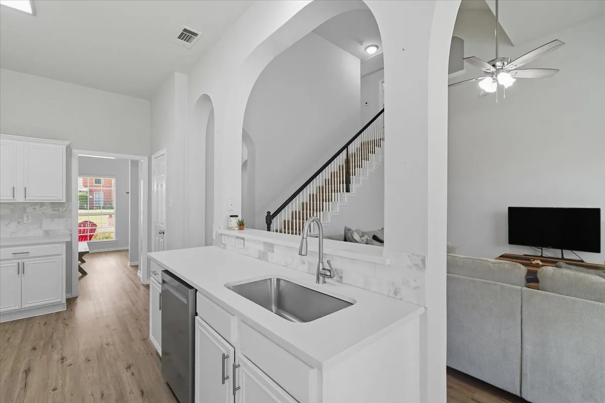 White shaker cabinetry, light wood-finish flooring, stainless steel sink, contemporary faucet, and white countertops