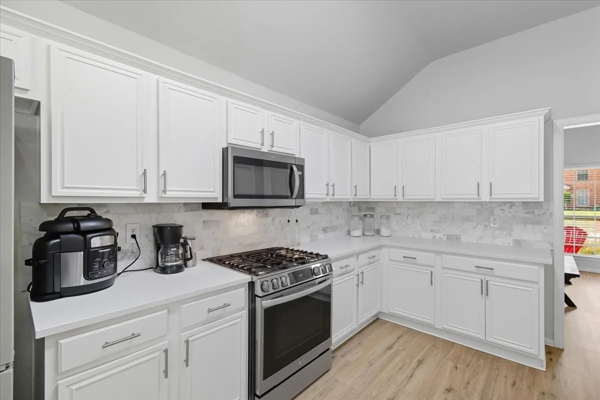 Kitchen featuring white cabinetry, stainless steel appliances, light-toned countertops, tile backsplash, and wood-finish flooring