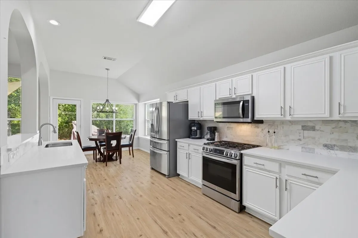 White cabinetry with brushed nickel hardware, stainless steel appliances, light wood-finish flooring, white countertops, and a vaulted ceiling