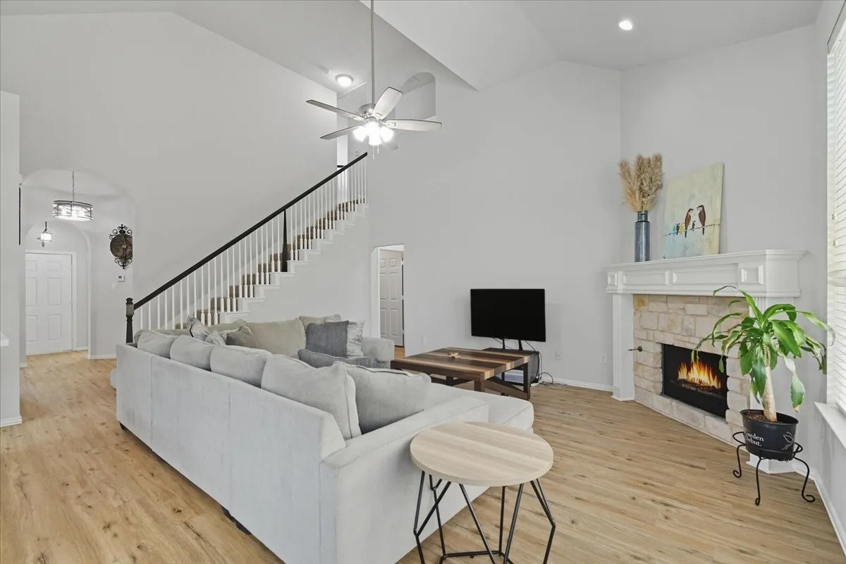 Vaulted ceiling with a ceiling fan, stone-surround fireplace with mantel, and wood-finish flooring