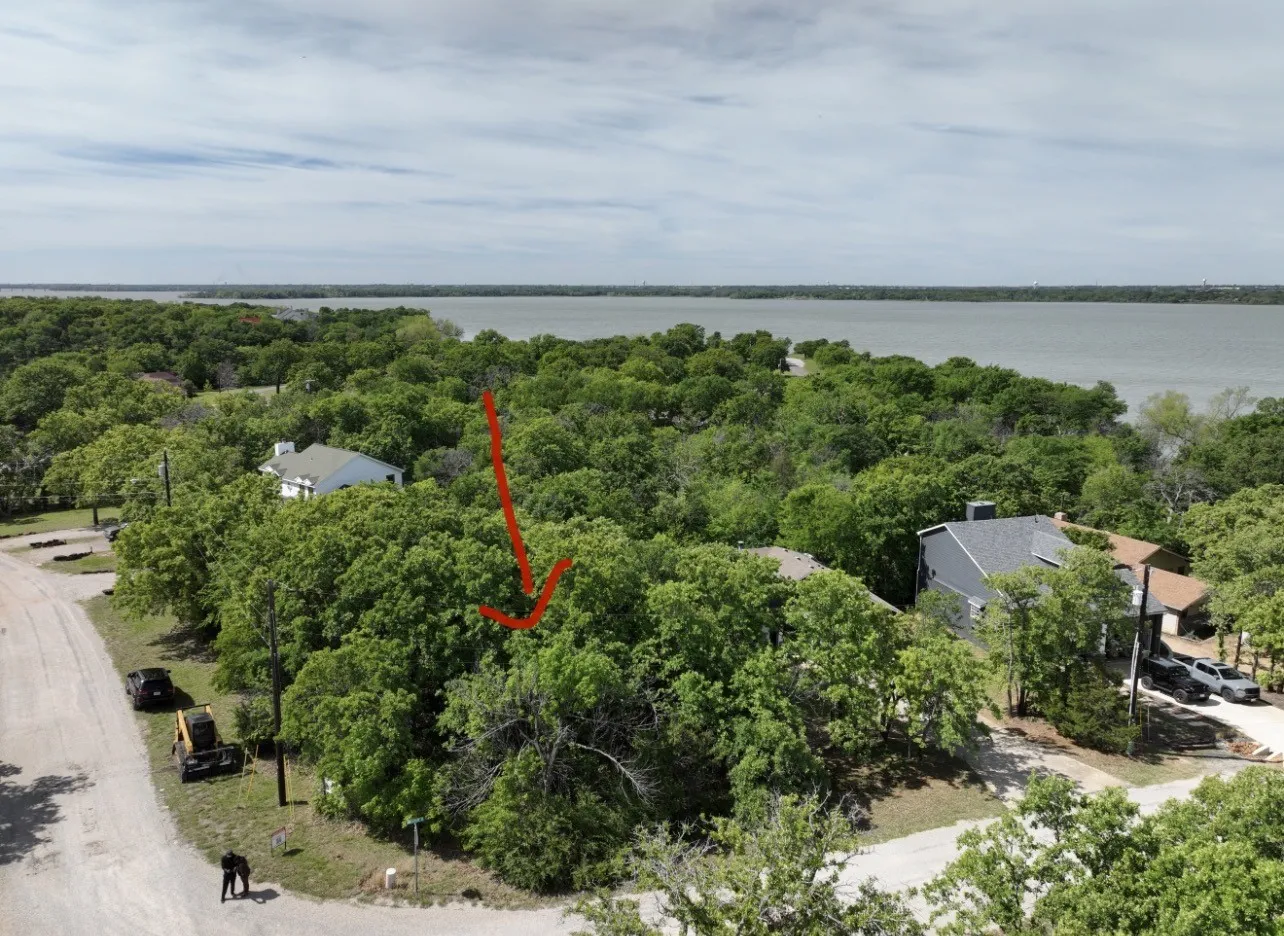 Waterfront property featuring mature tree canopy, expansive grounds with multiple structures, and panoramic water vistas across the landscape
