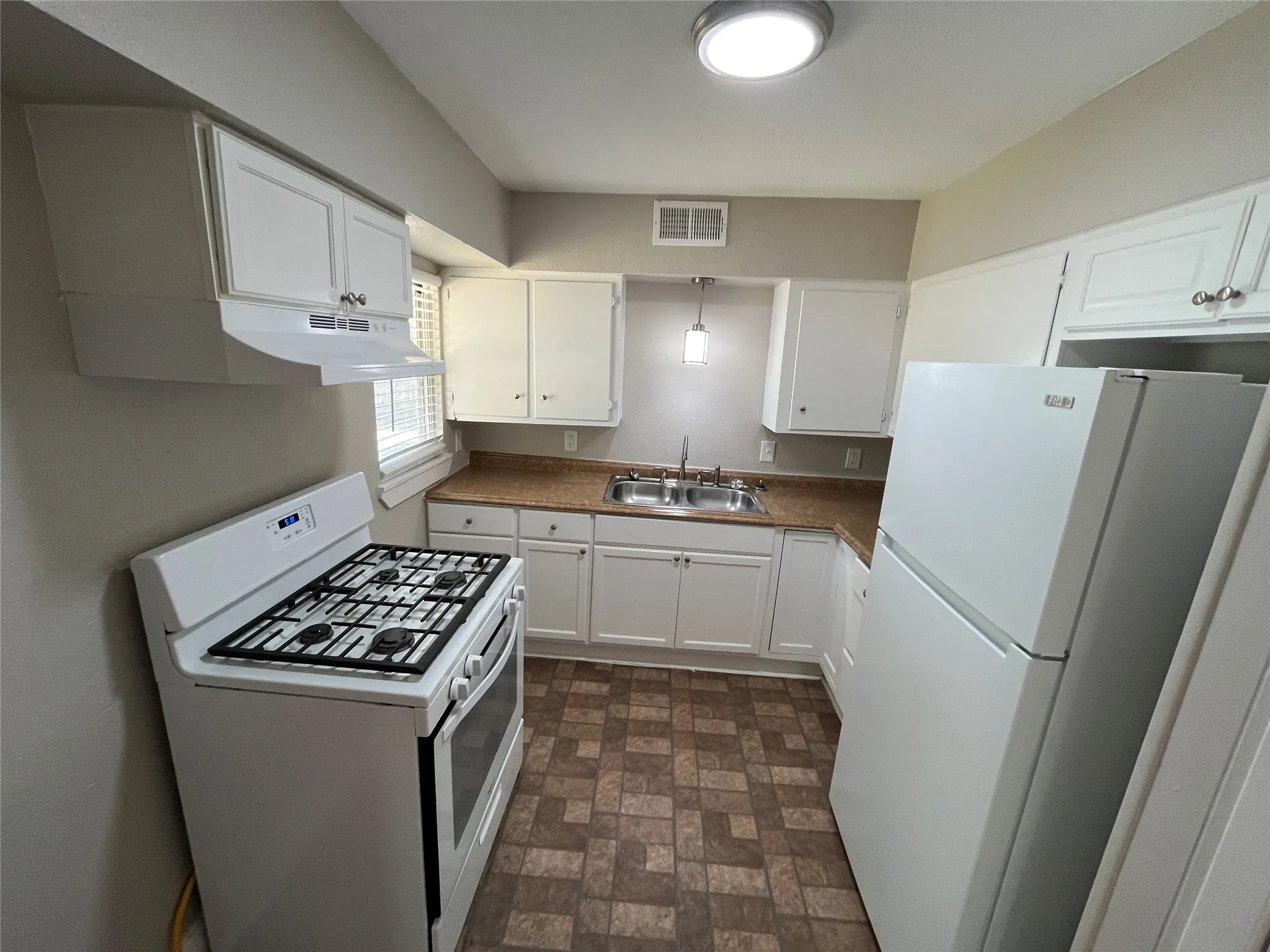 Efficient galley kitchen featuring white cabinetry, wood-finish countertops, a gas cooktop, and stainless steel appliances including refrigerator and range