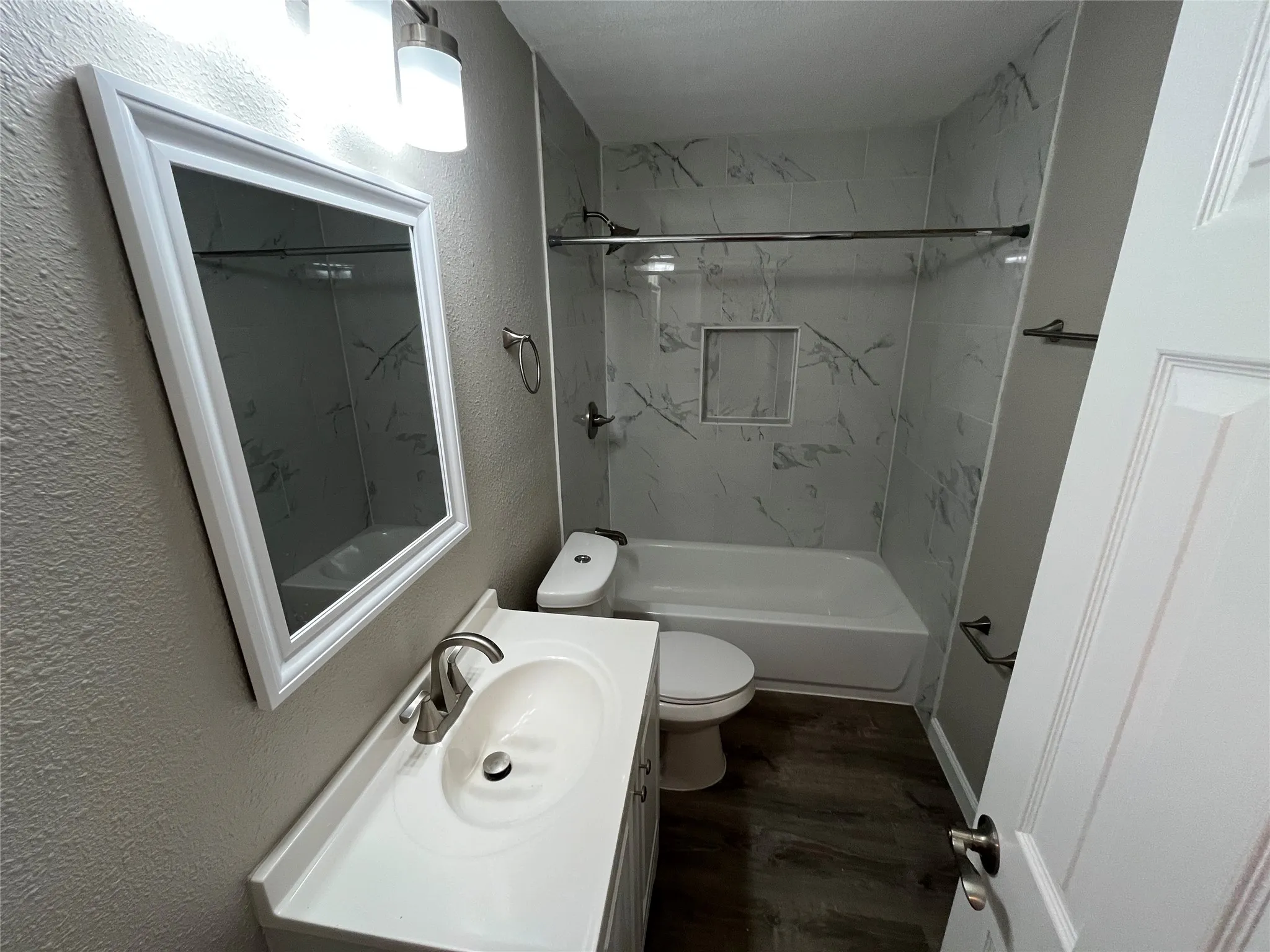 Updated full bathroom featuring a ceramic pedestal sink with chrome faucet, white ceramic toilet, and an enclosed shower-tub combination with marble-look tile surround and glass enclosure