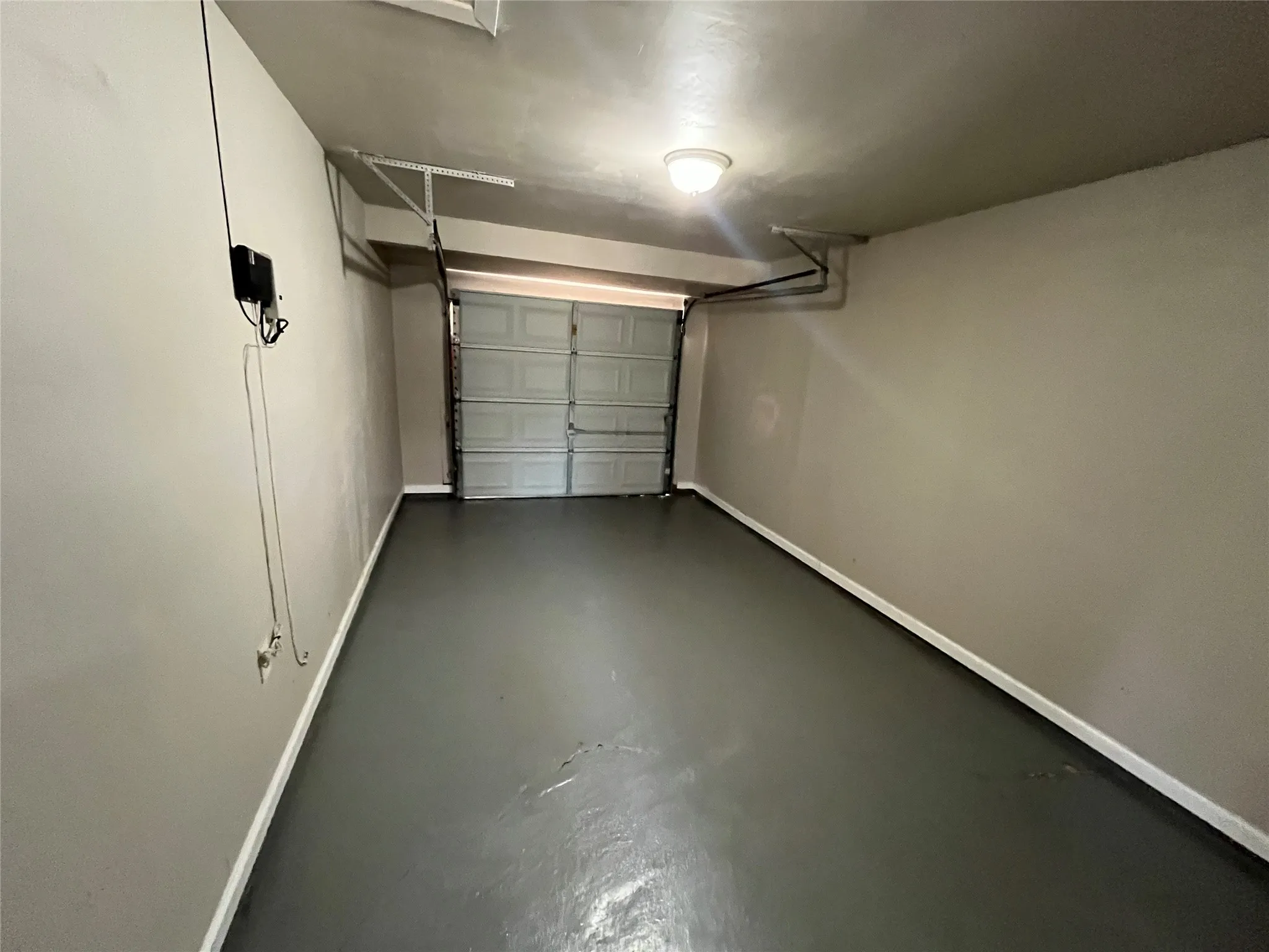Spacious garage featuring a sealed concrete floor, overhead garage door with automatic opener, wall-mounted electrical panel, and bright overhead lighting