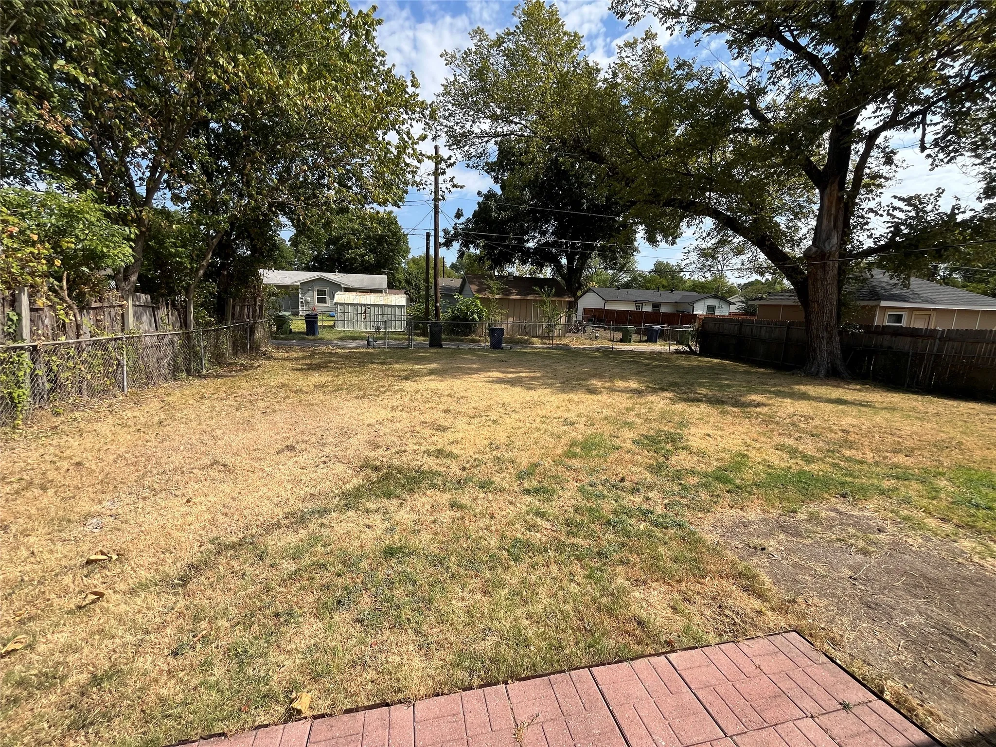 Spacious backyard with mature shade trees, brick patio foundation, and level grounds ideal for outdoor entertaining or expansion