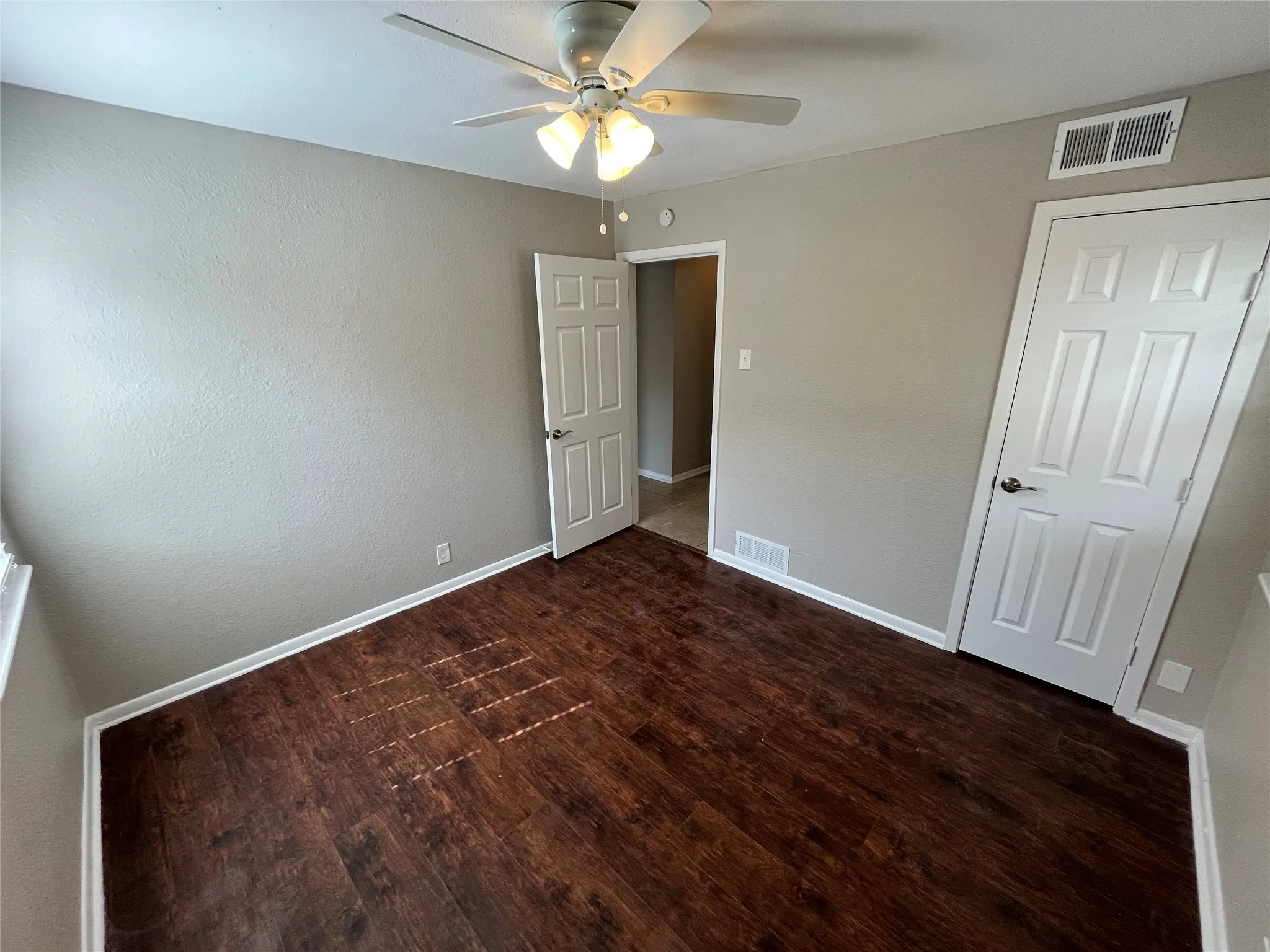 Spacious bedroom featuring rich wood-finish flooring, neutral wall finishes, and ceiling fan with integrated lighting
